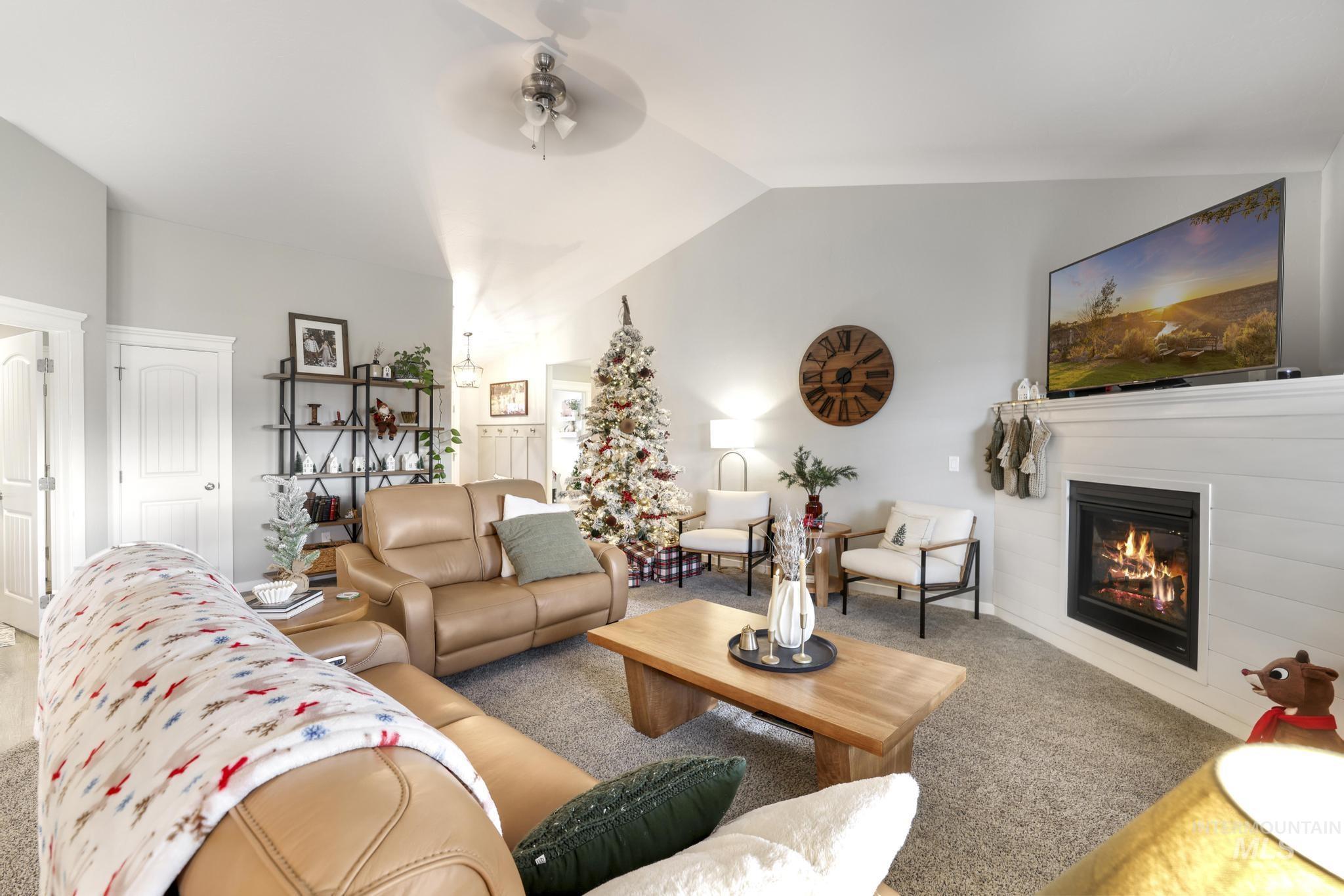 Living room with carpet, a ceiling fan, a glass covered fireplace, and lofted ceiling