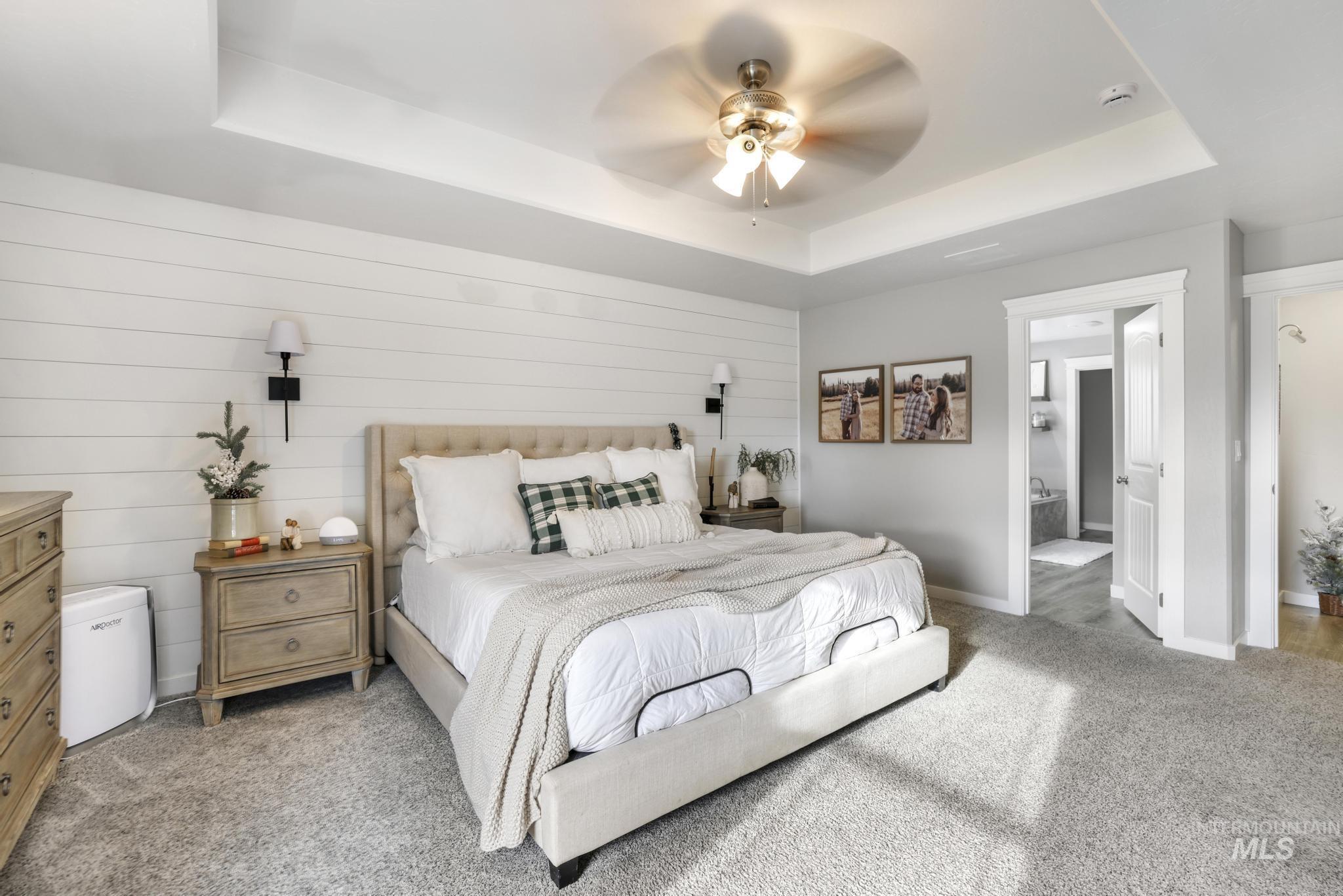 Bedroom with carpet floors, ceiling fan, a raised ceiling, and wooden walls