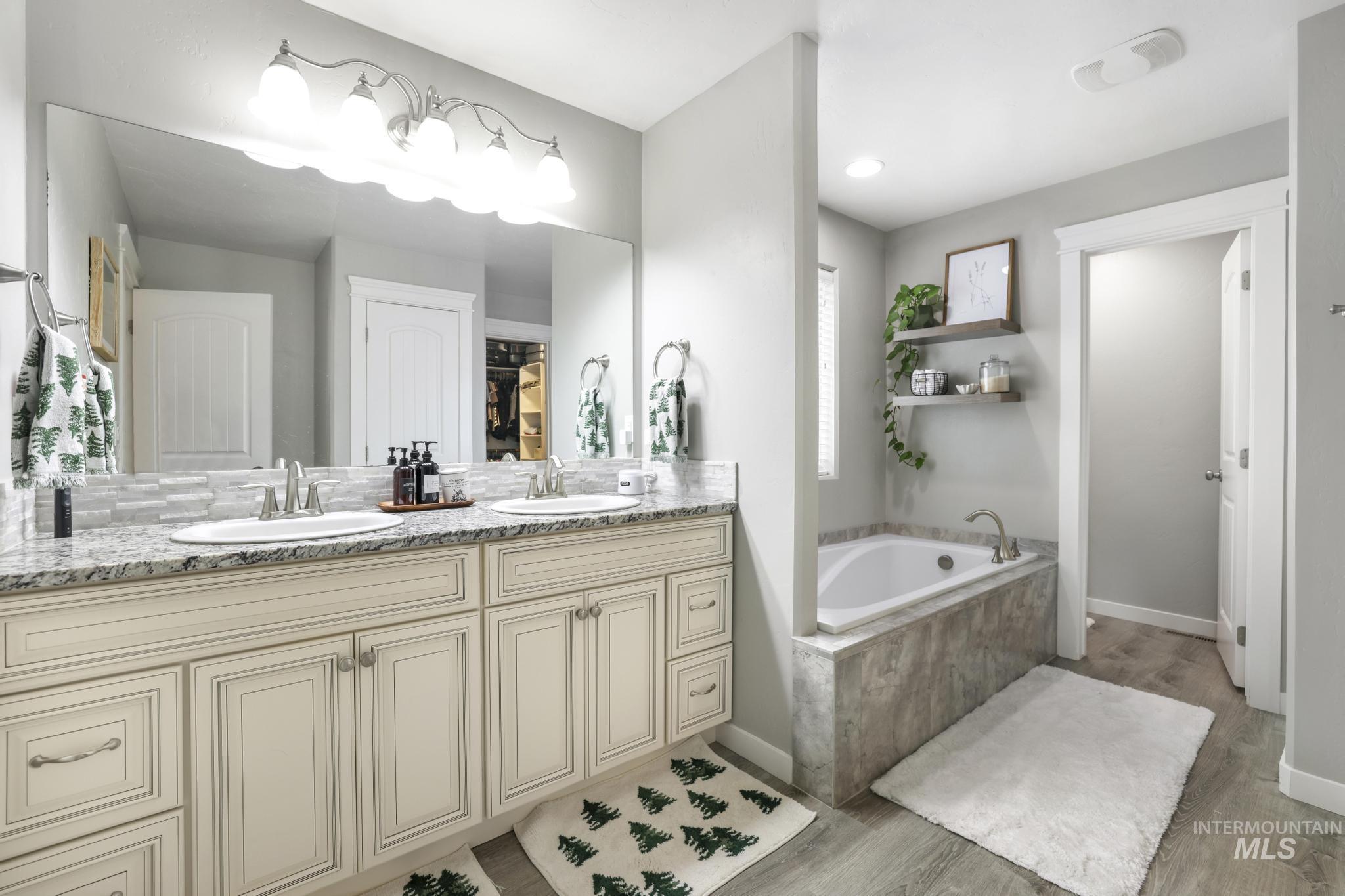Full bathroom with double vanity, a bath, and light wood-type flooring