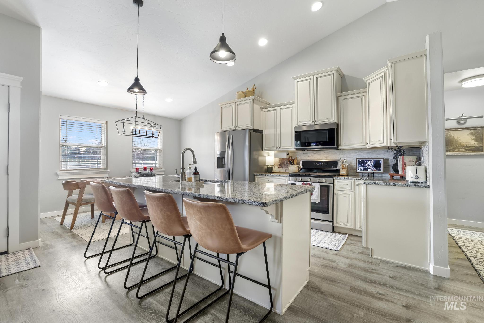 Kitchen with dark stone counters, a kitchen bar, appliances with stainless steel finishes, vaulted ceiling, and a kitchen island with sink