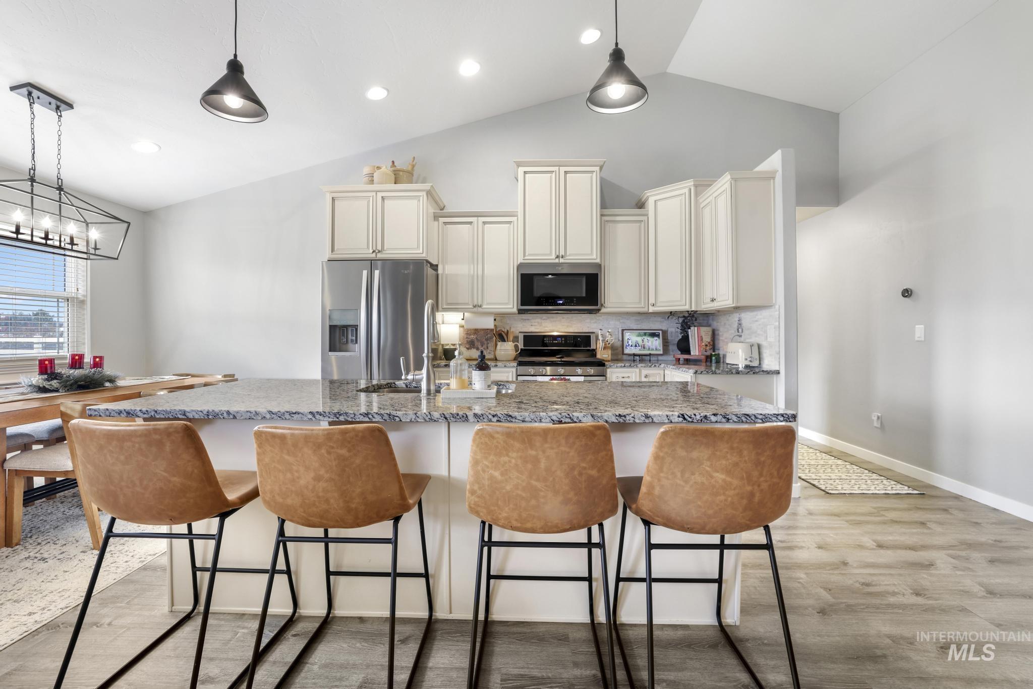 Kitchen featuring vaulted ceiling, stainless steel appliances, light stone countertops, a kitchen breakfast bar, and a center island with sink