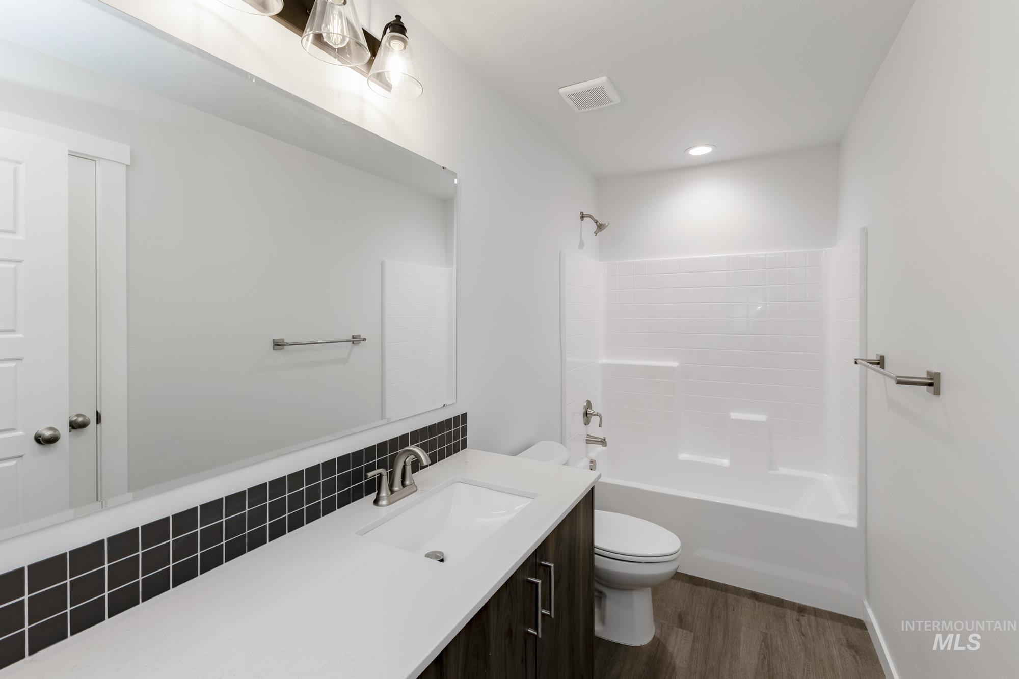 Full bath featuring vanity,  shower combination, dark wood-type flooring, and decorative backsplash
