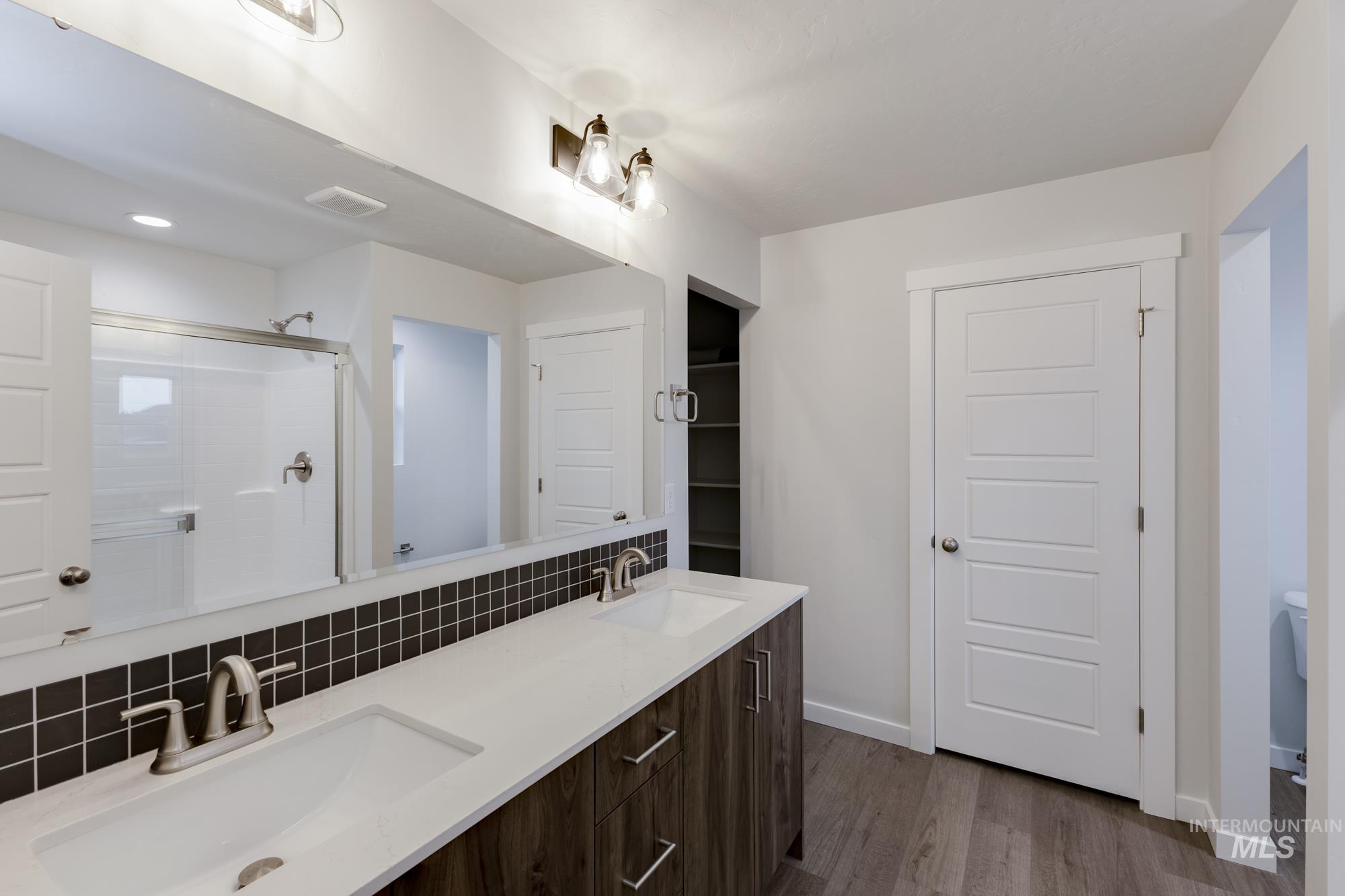 Bathroom featuring double vanity, backsplash, a stall shower, and dark wood finished floors