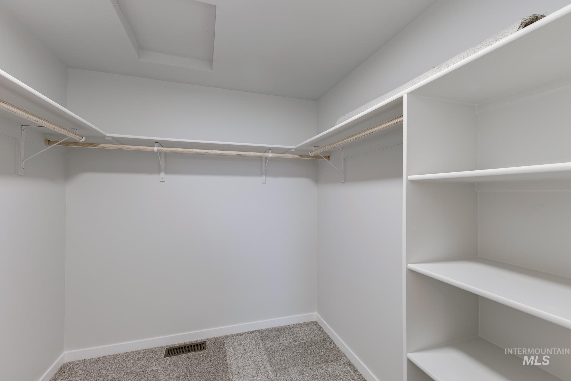 Walk in closet with light colored carpet and attic access