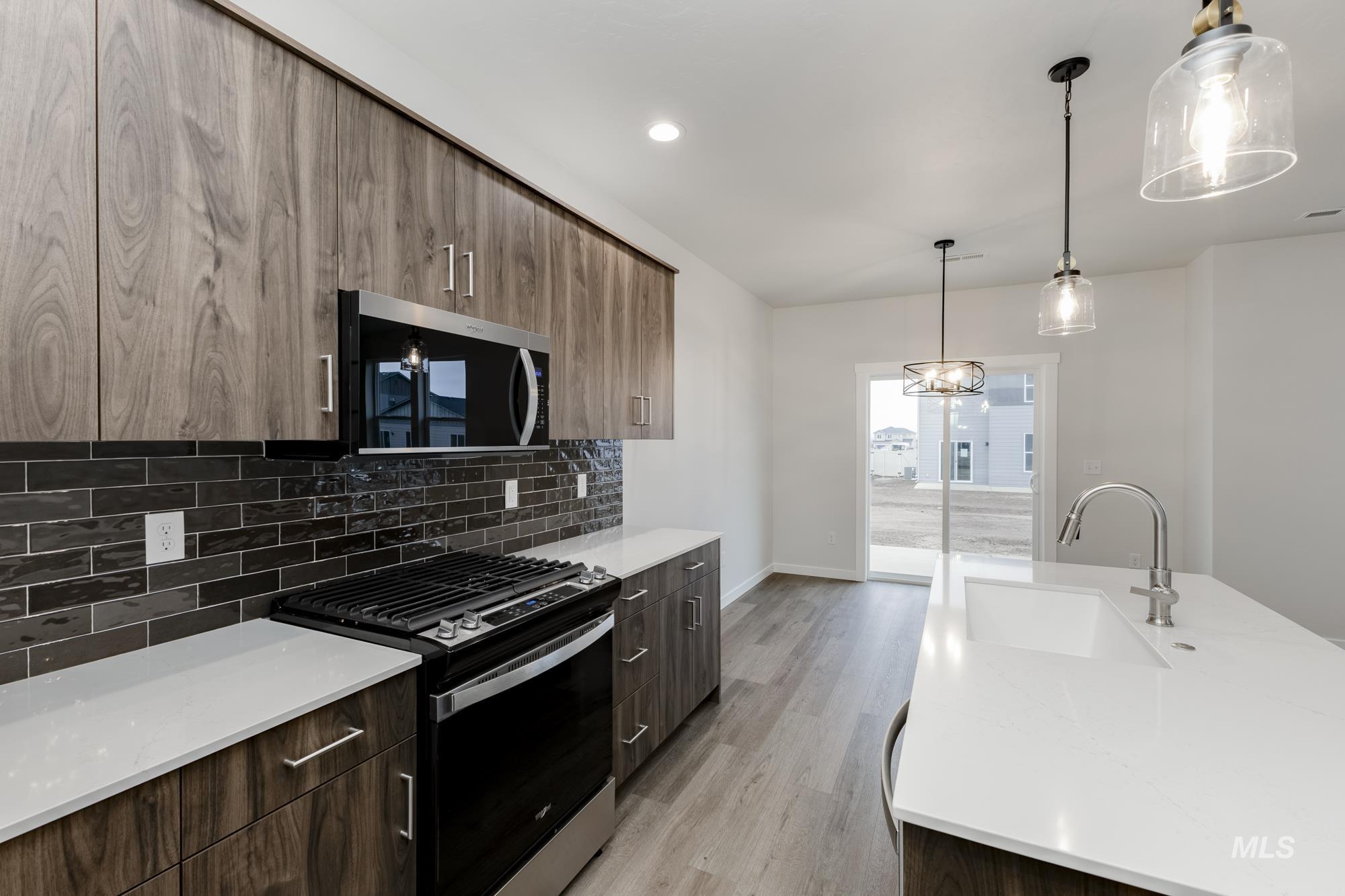Kitchen featuring black gas stove, pendant lighting, stainless steel microwave, light stone countertops, and backsplash