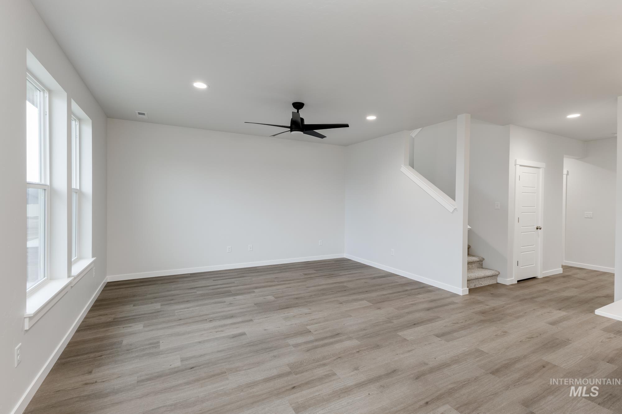 Unfurnished living room featuring light wood finished floors, ceiling fan, stairway, and recessed lighting