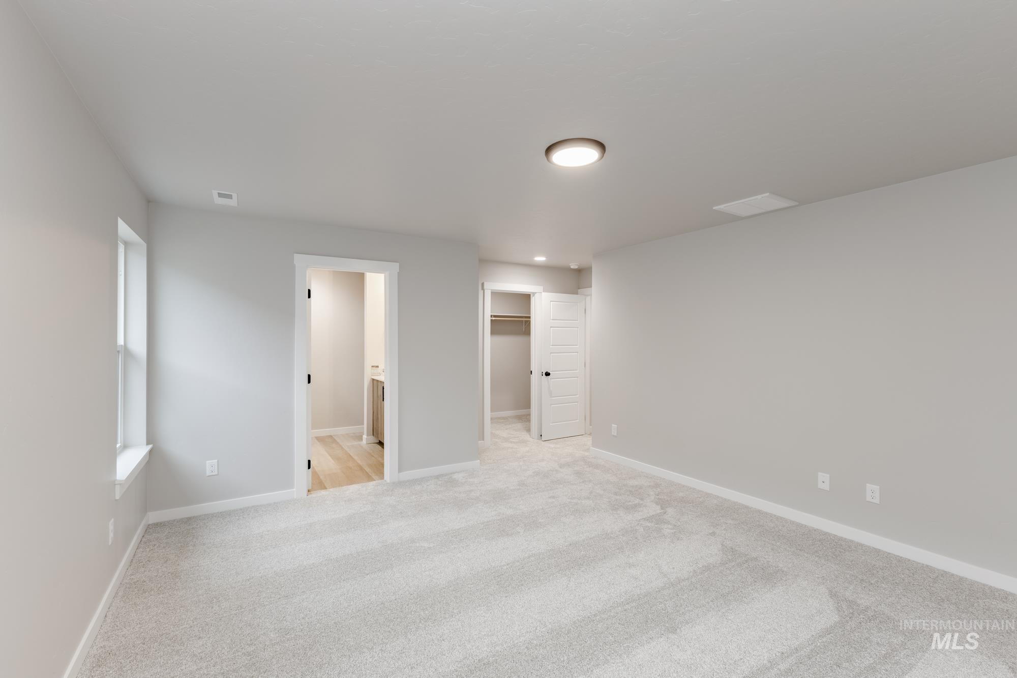 Unfurnished bedroom with connected bathroom, light colored carpet, and a spacious closet