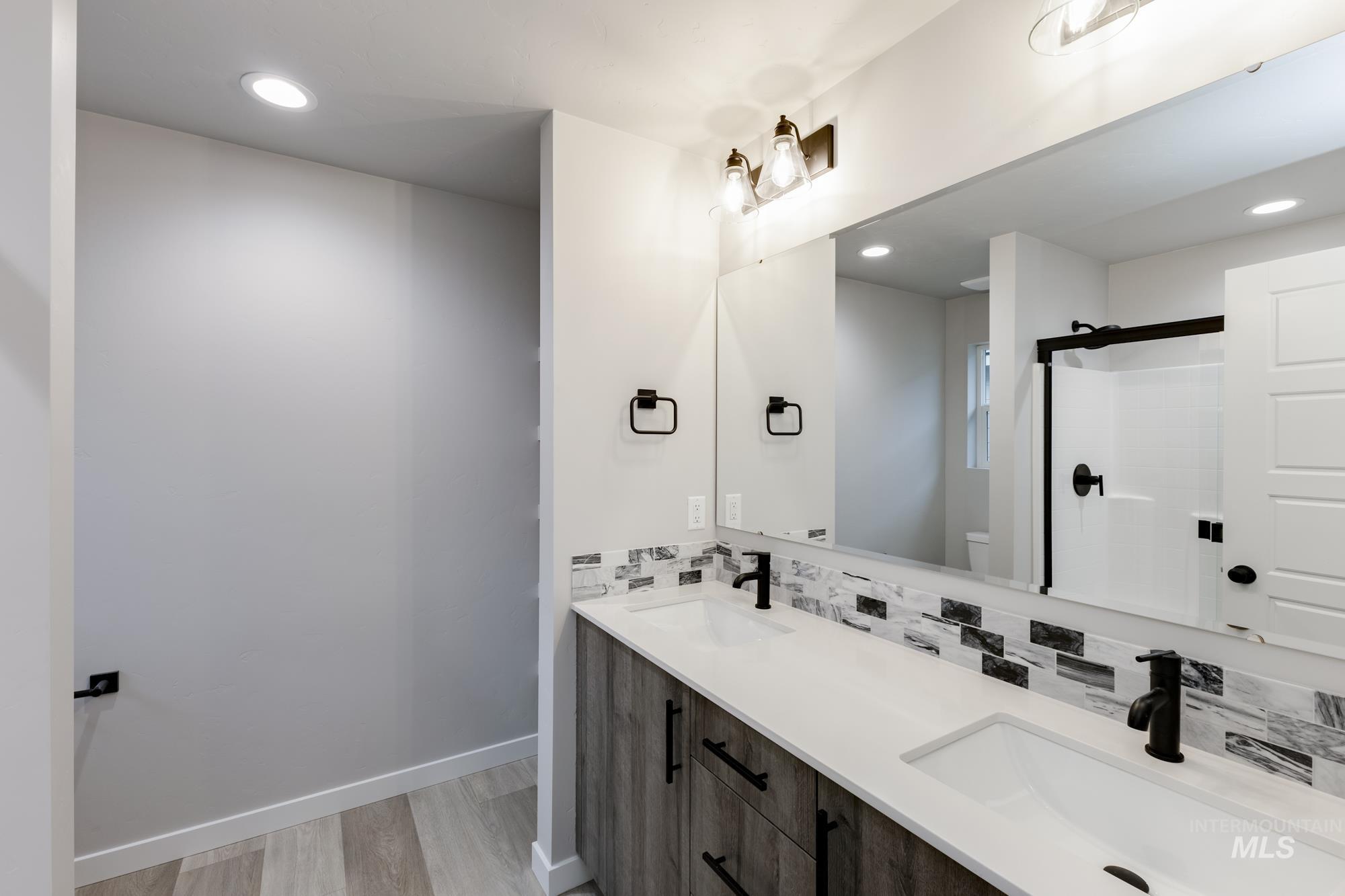 Bathroom with recessed lighting, double vanity, tasteful backsplash, a shower stall, and light wood-style flooring