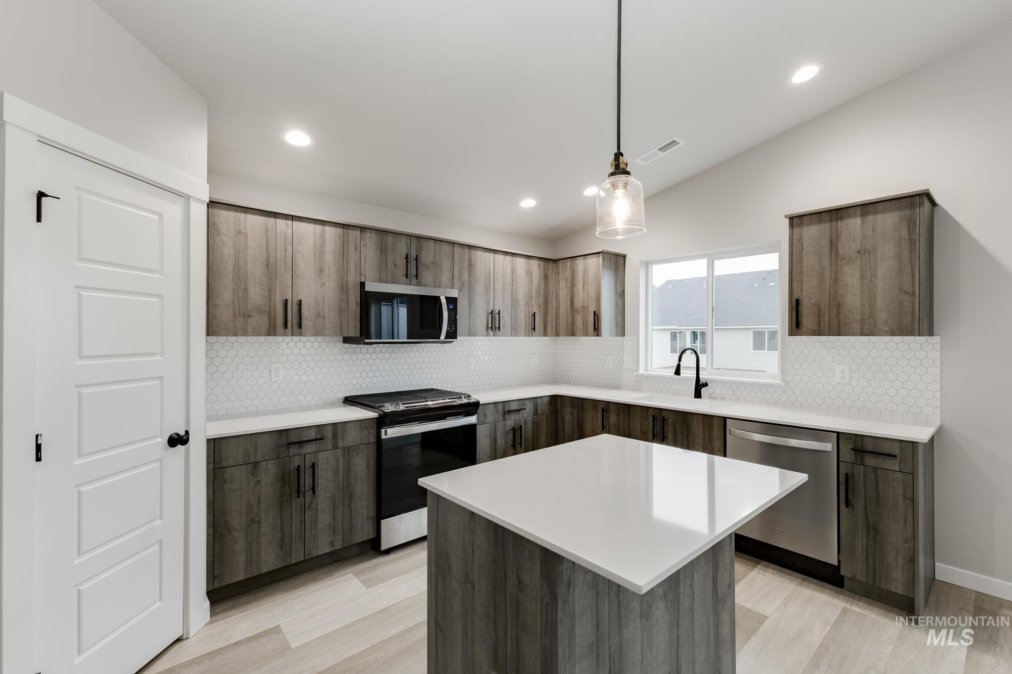 Kitchen with modern cabinets, appliances with stainless steel finishes, hanging light fixtures, decorative backsplash, and recessed lighting