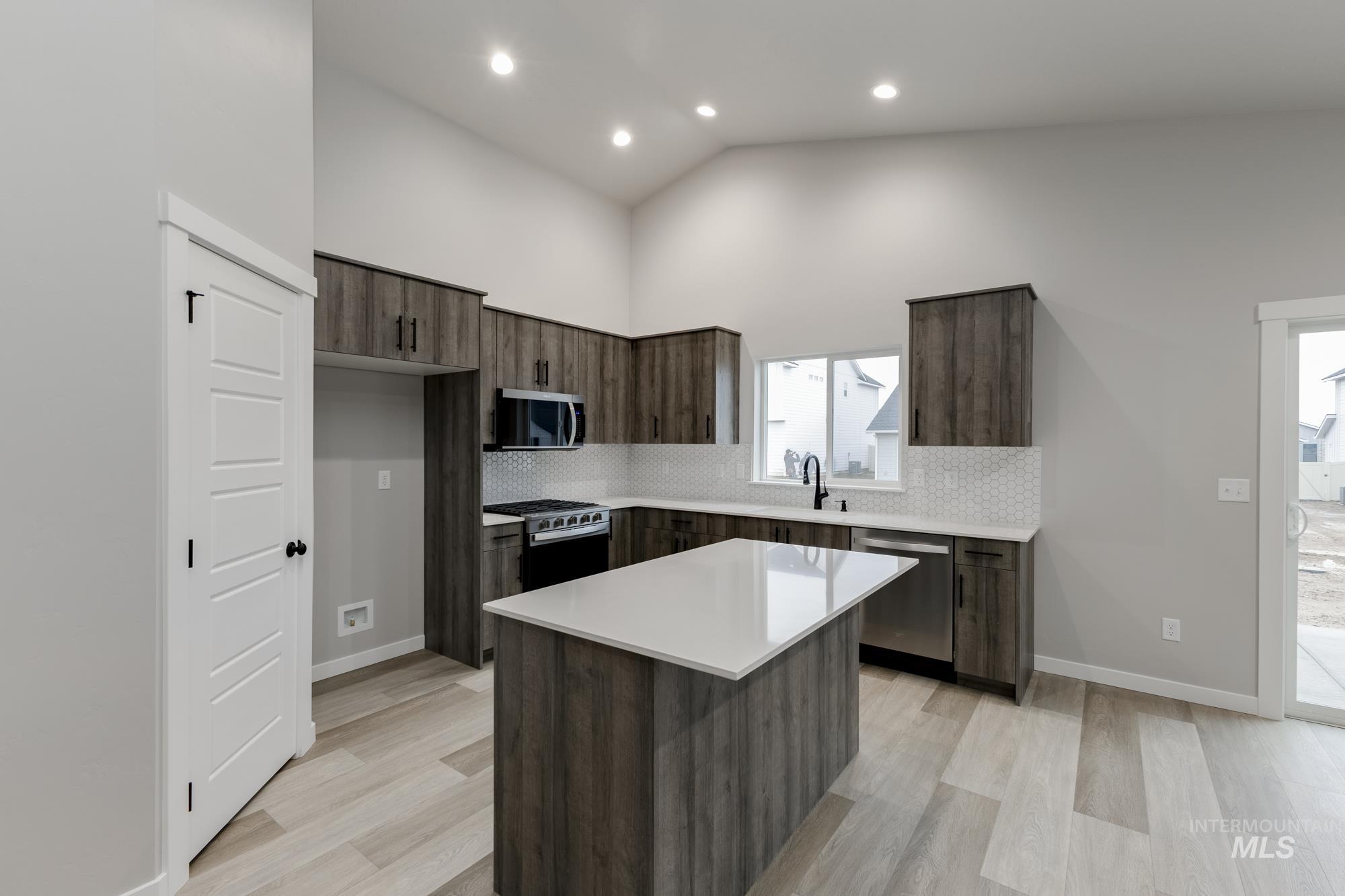 Kitchen with modern cabinets, dark brown cabinetry, appliances with stainless steel finishes, light wood finished floors, and recessed lighting