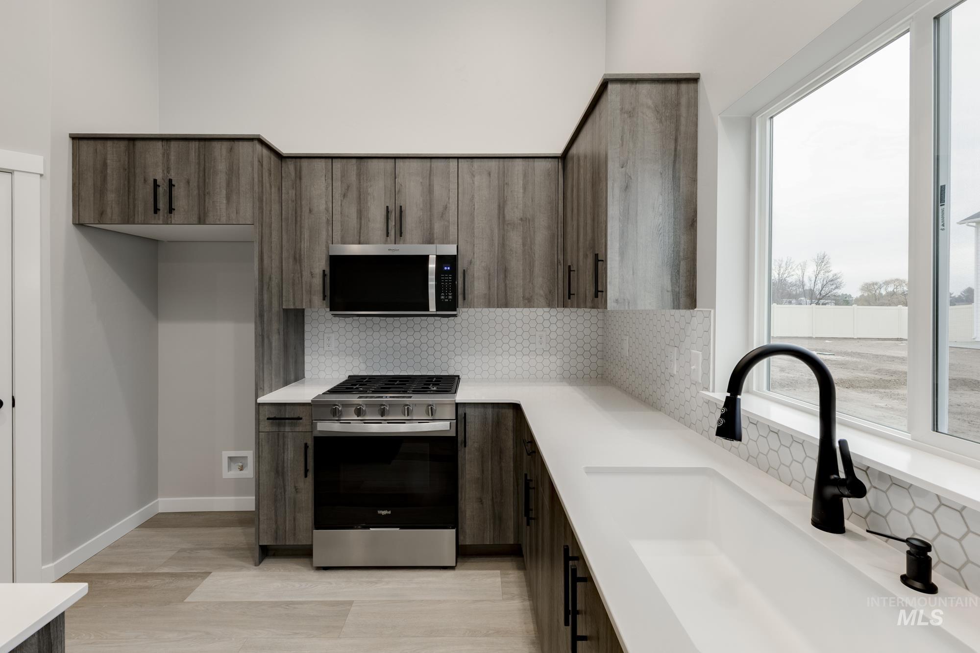 Kitchen featuring stainless steel appliances, decorative backsplash, modern cabinets, light wood finished floors, and dark brown cabinets