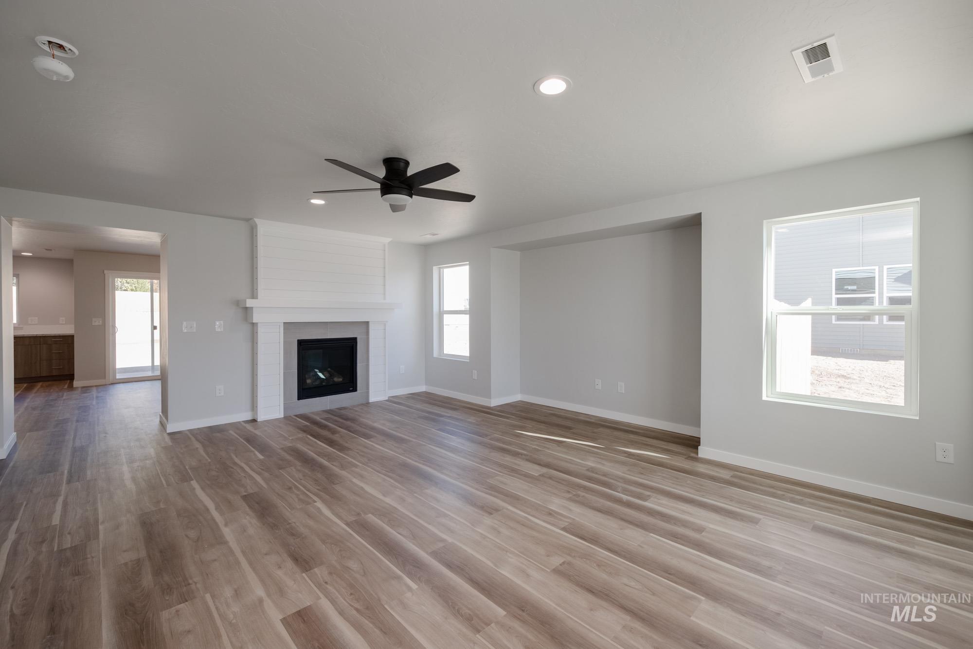 Unfurnished living room featuring a ceiling fan, light wood finished floors, plenty of natural light, recessed lighting, and a fireplace
