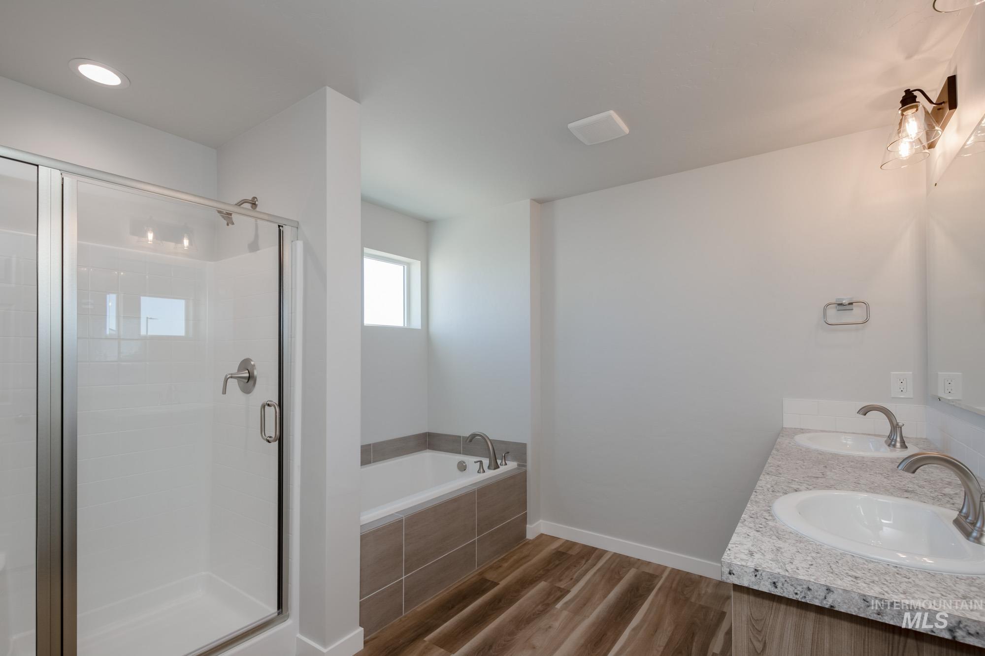Full bathroom featuring double vanity, dark wood finished floors, a stall shower, and a garden tub