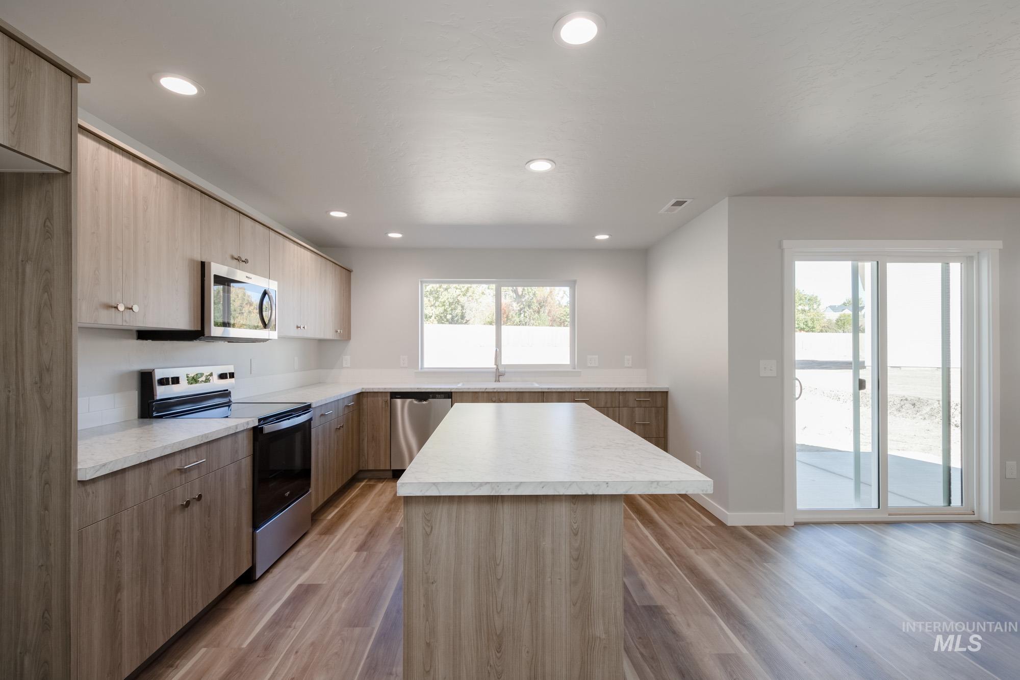 Kitchen featuring appliances with stainless steel finishes, light countertops, modern cabinets, a kitchen island, and light wood-type flooring