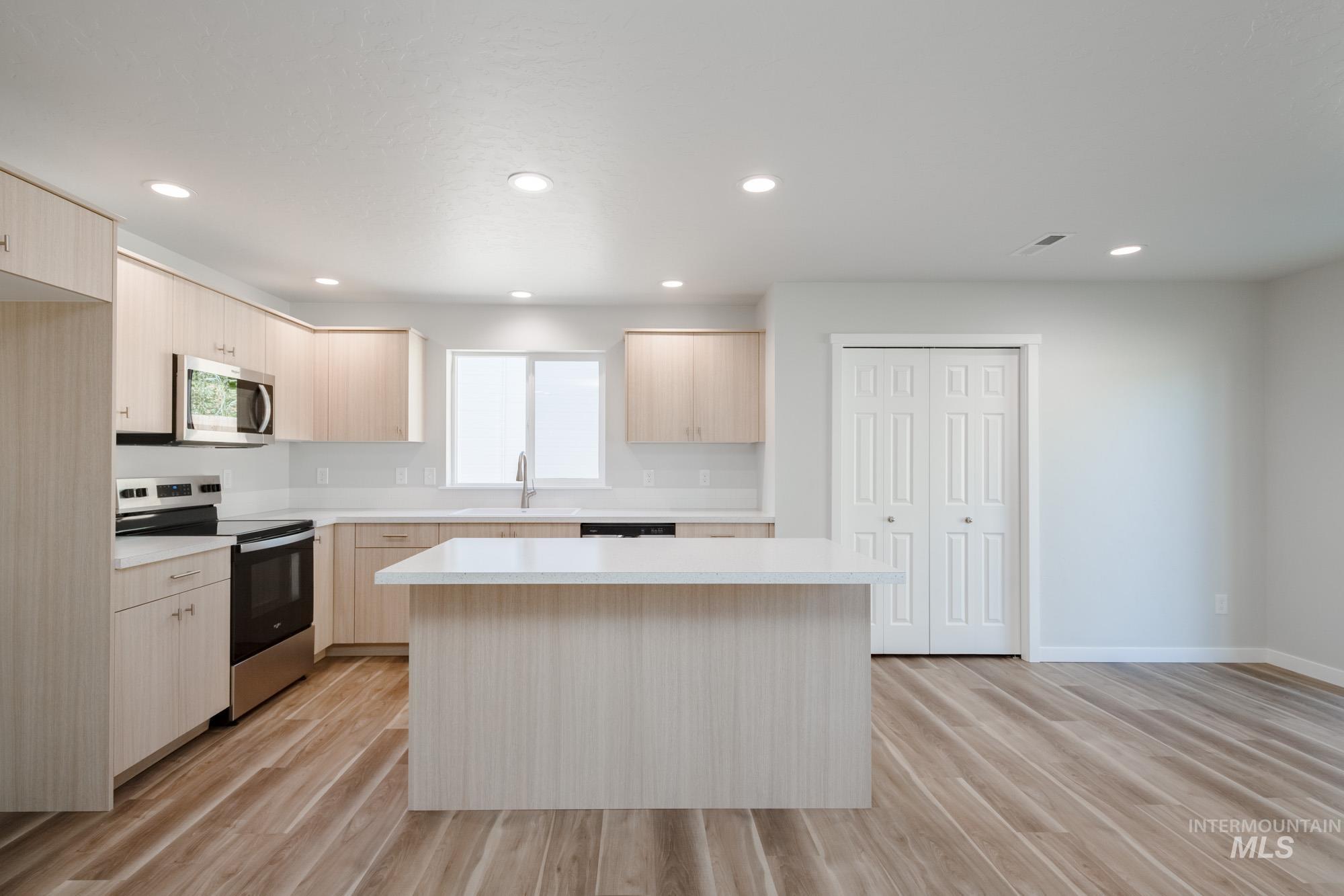 Kitchen with light brown cabinets, appliances with stainless steel finishes, light countertops, modern cabinets, and light wood-type flooring