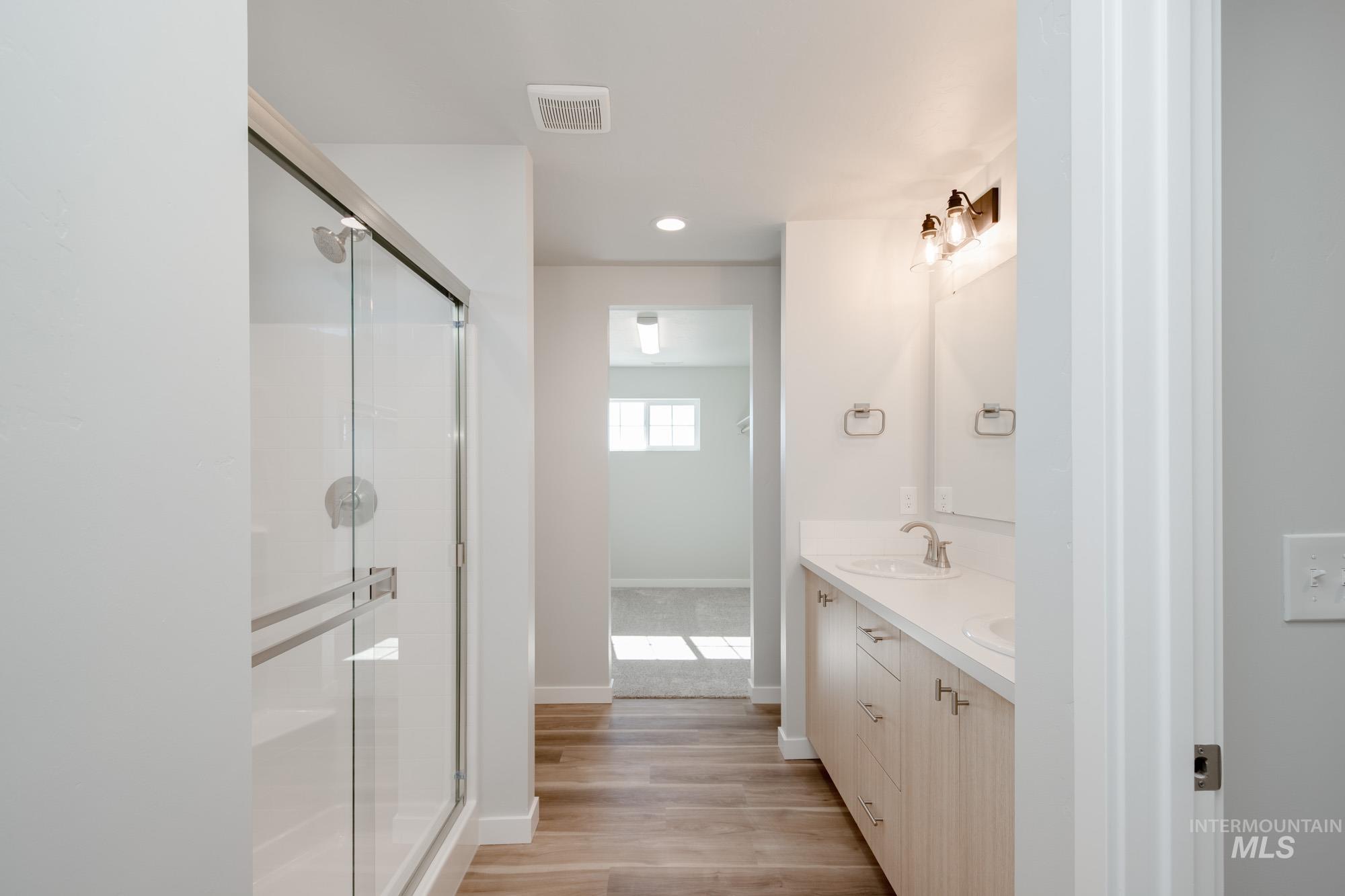 Bathroom with double vanity, light wood-style flooring, a shower stall, and recessed lighting