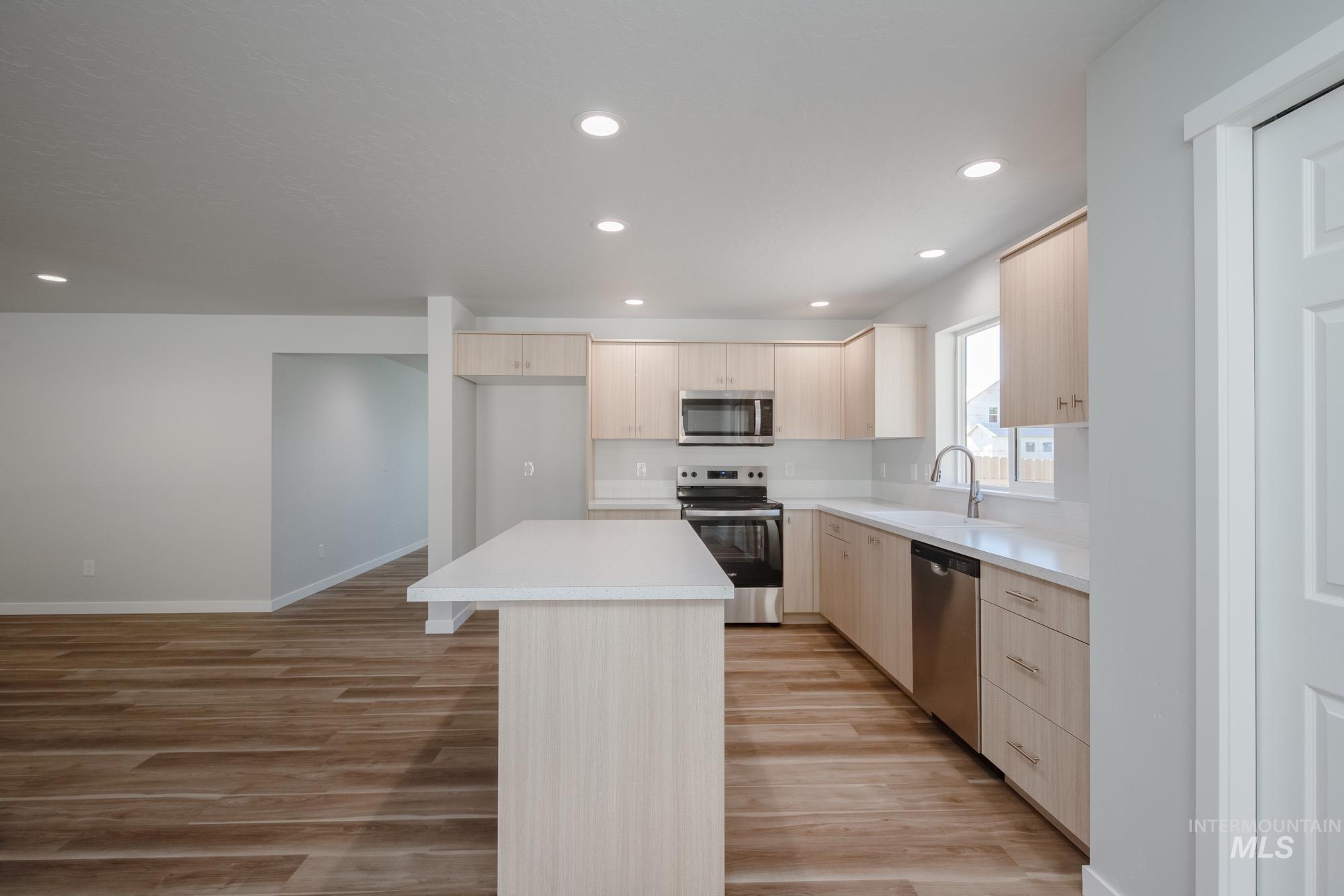 Kitchen with light brown cabinetry, appliances with stainless steel finishes, recessed lighting, a center island, and light wood finished floors