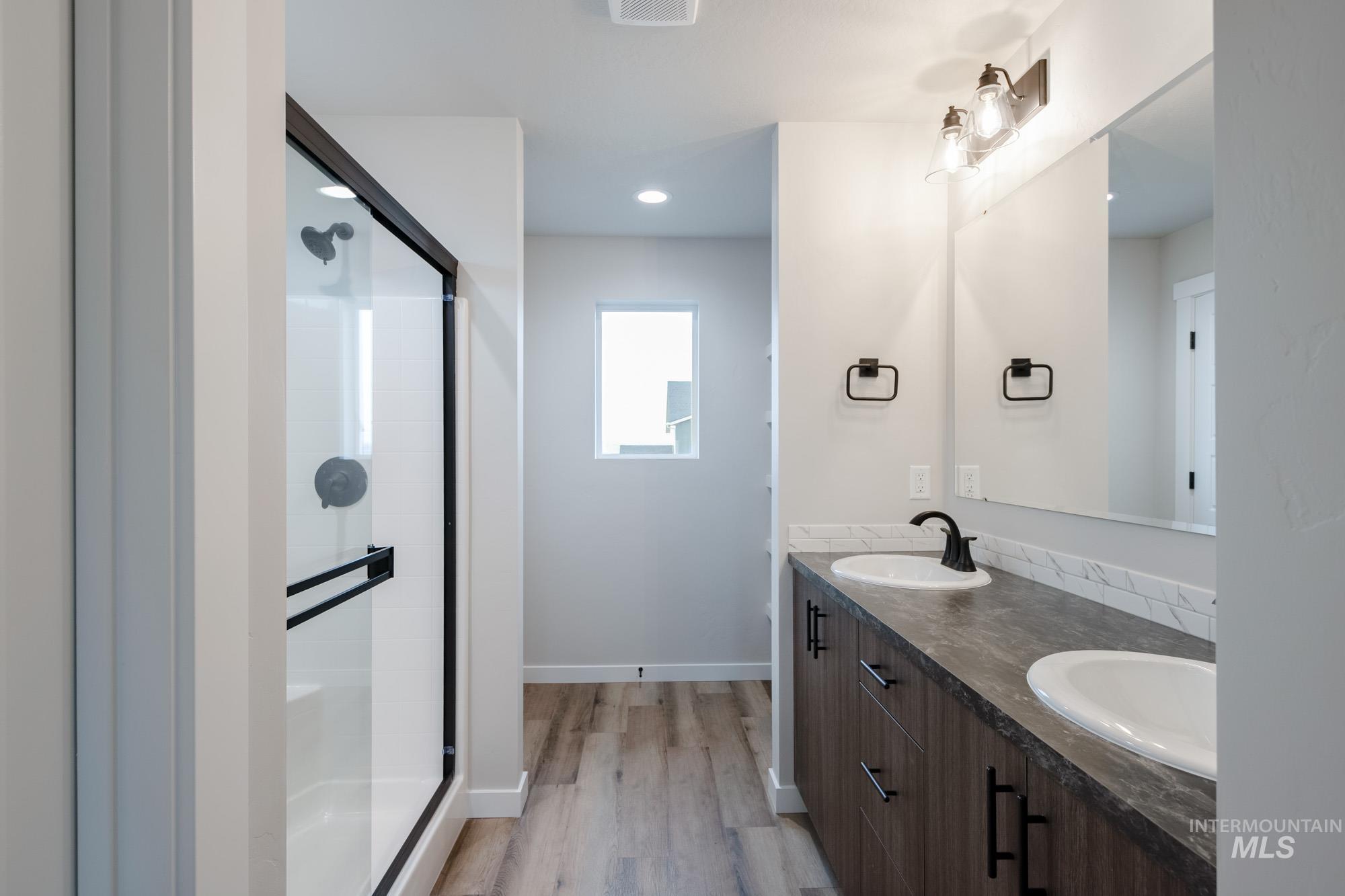 Bathroom featuring double vanity, a shower stall, light wood finished floors, and recessed lighting