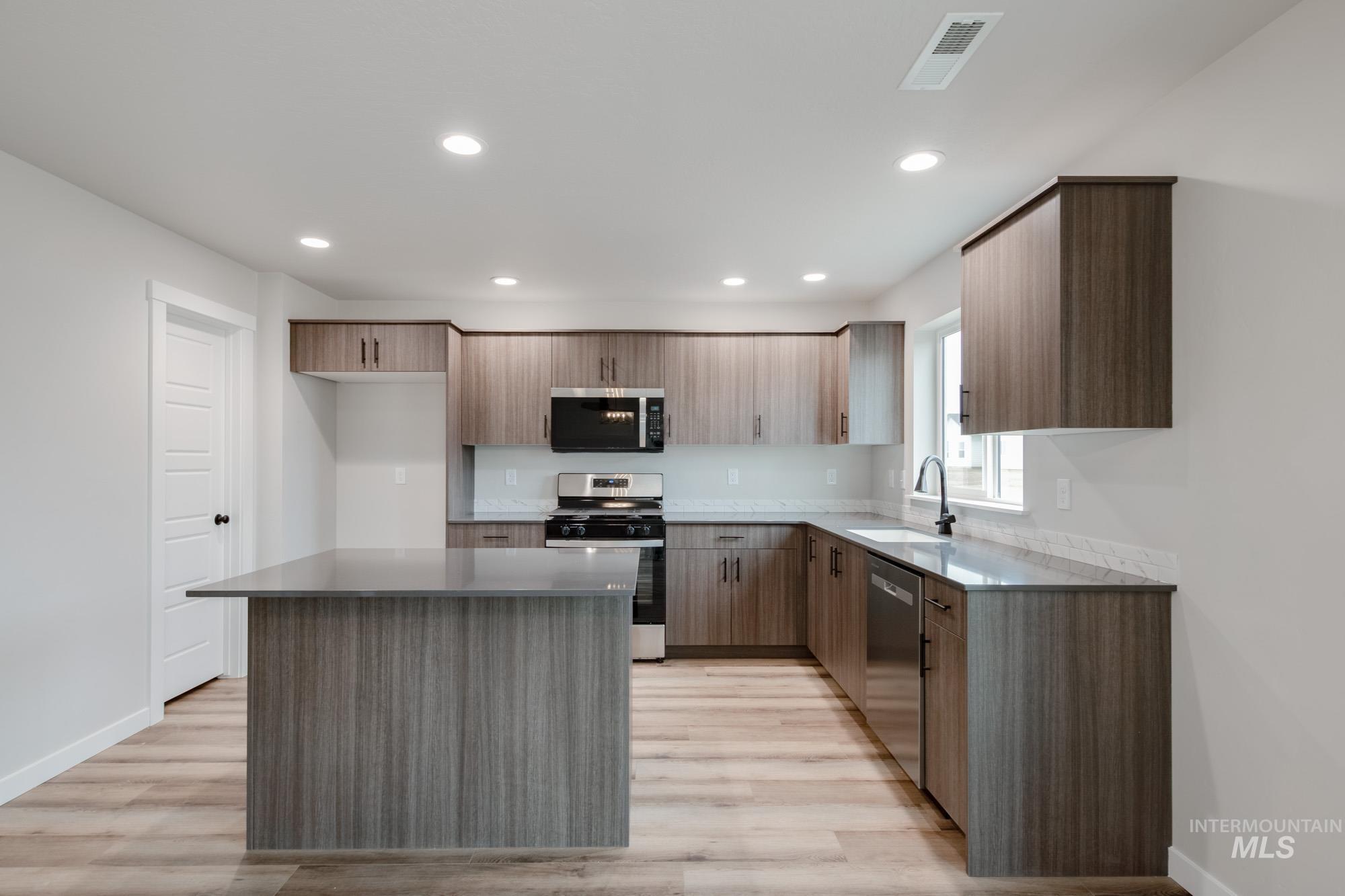 Kitchen with appliances with stainless steel finishes, dark stone countertops, modern cabinets, light wood-type flooring, and recessed lighting