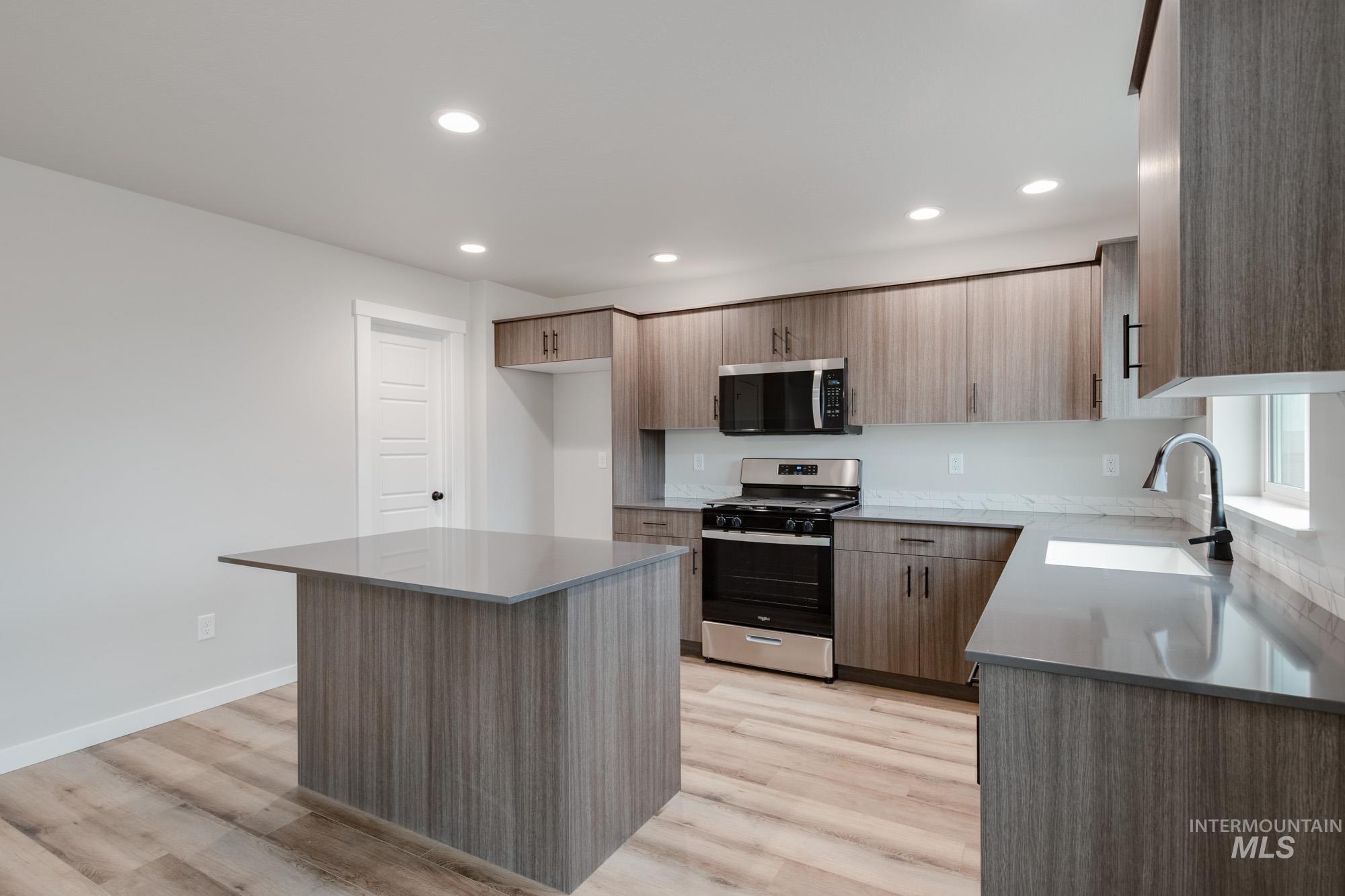 Kitchen with stainless steel appliances, recessed lighting, a center island, light stone counters, and light wood finished floors