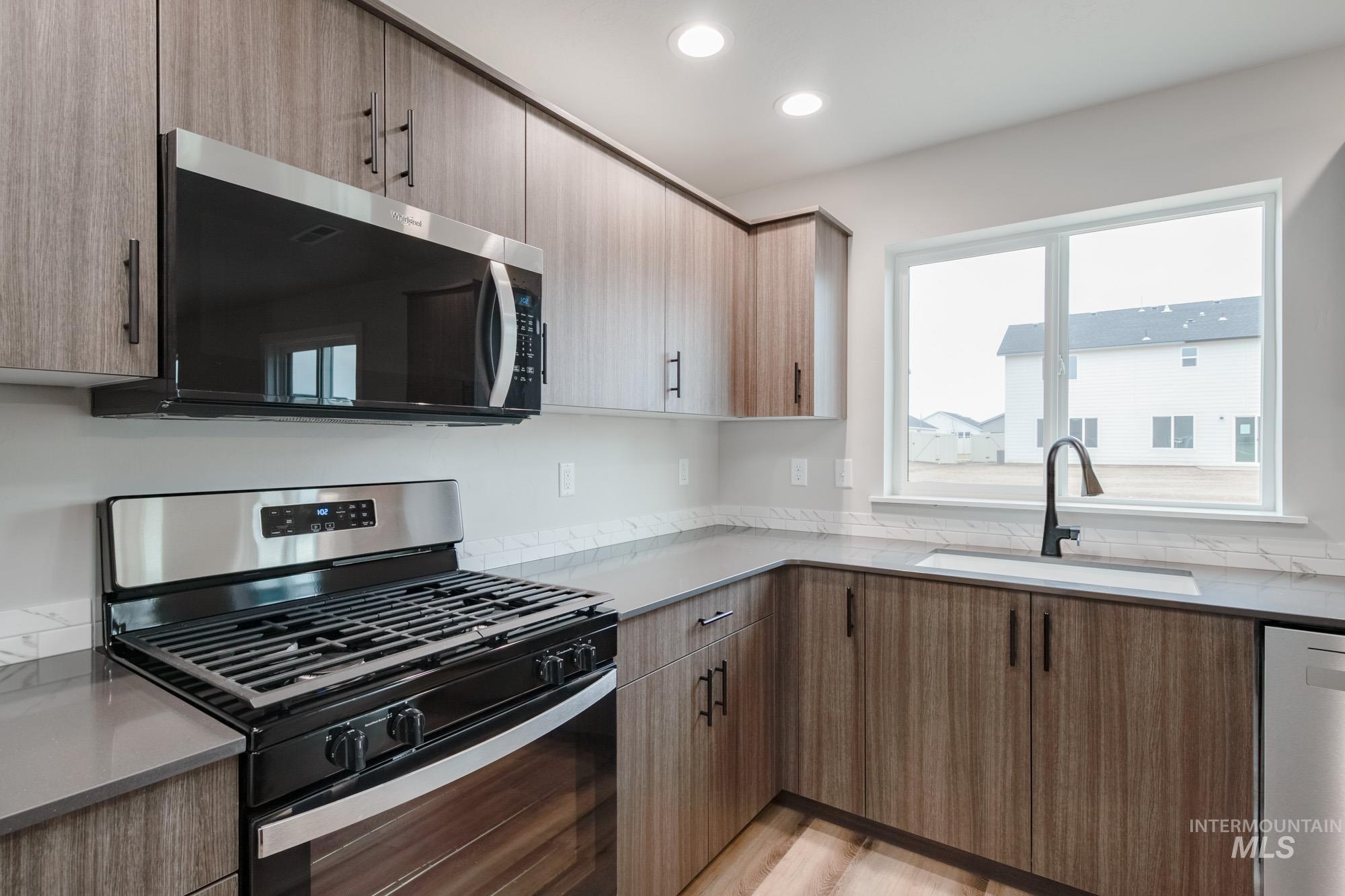 Kitchen with appliances with stainless steel finishes, recessed lighting, light stone counters, light wood finished floors, and modern cabinets