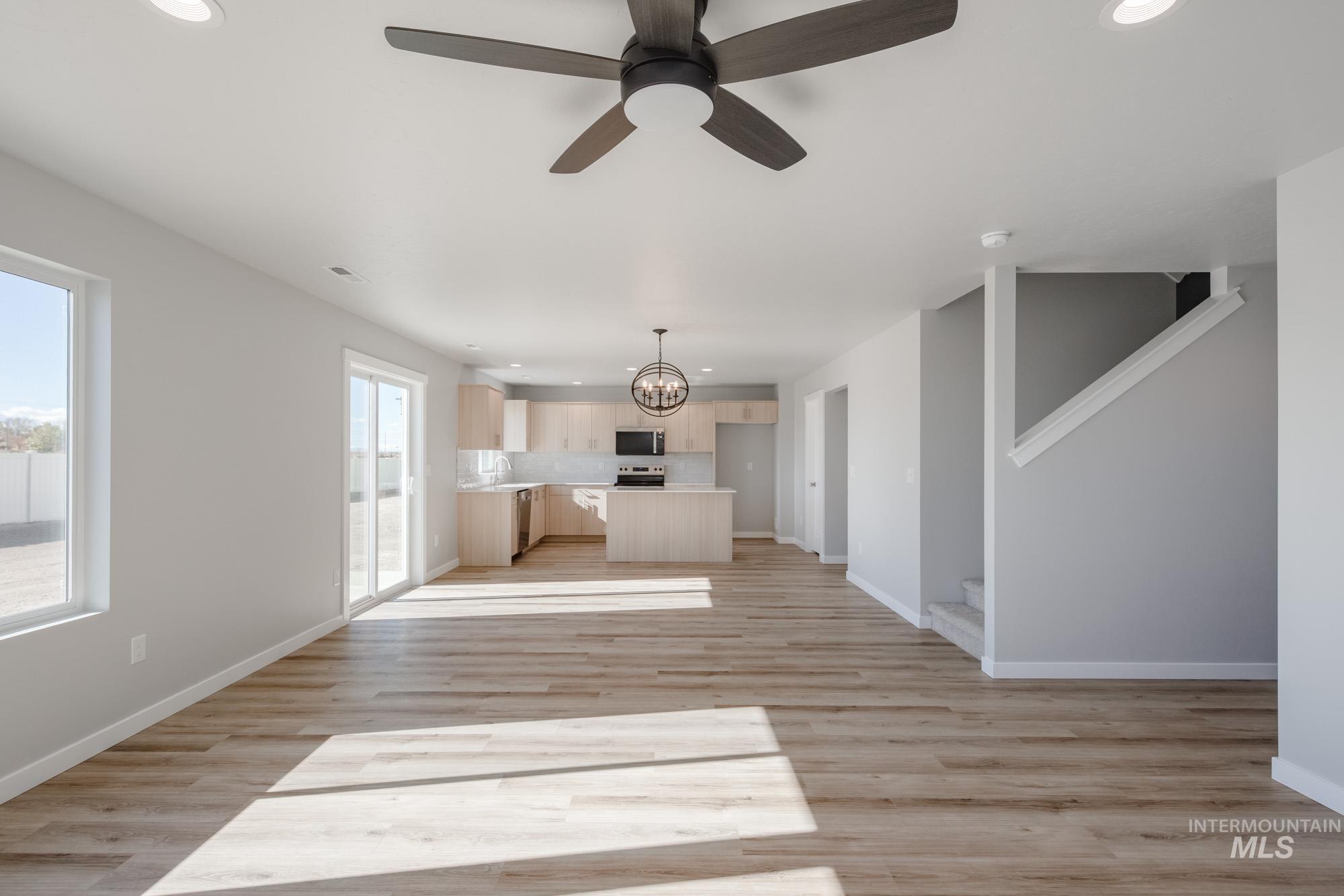 Unfurnished living room featuring recessed lighting, light wood-style flooring, a chandelier, ceiling fan, and stairs