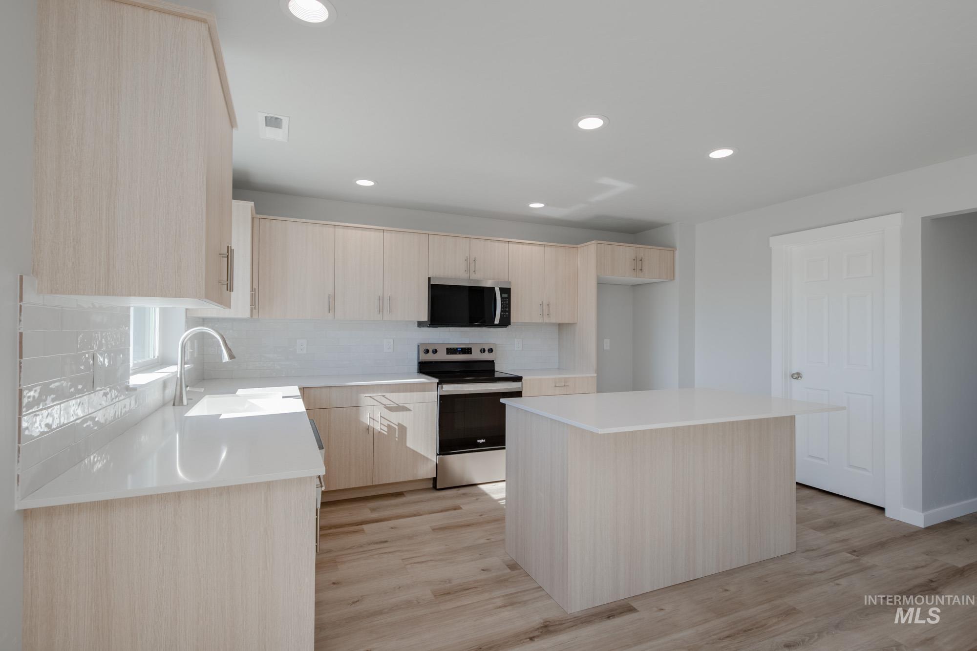Kitchen featuring light brown cabinets, decorative backsplash, stainless steel appliances, recessed lighting, and a center island
