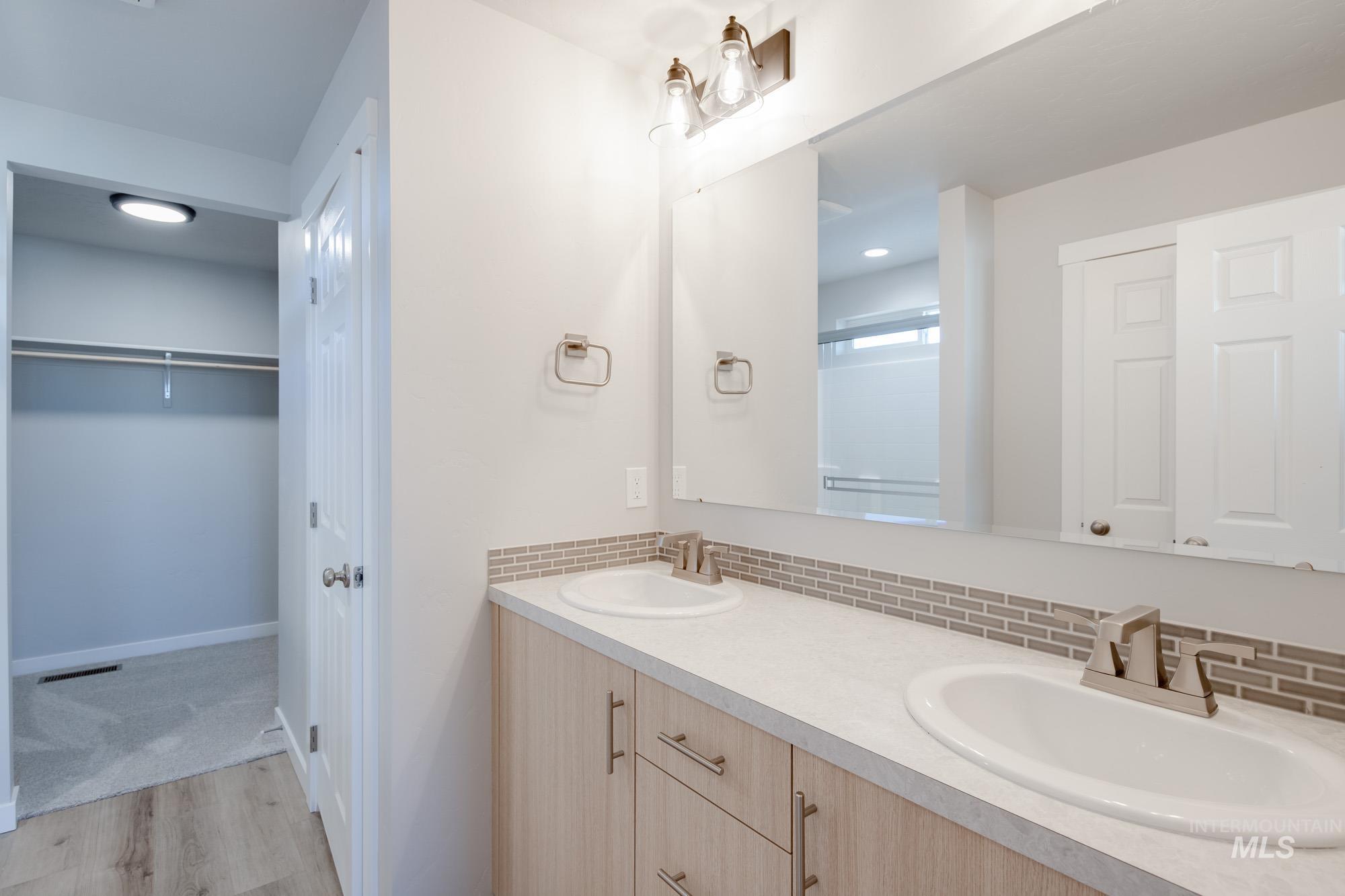 Bathroom featuring light wood-style flooring, double vanity, a spacious closet, decorative backsplash, and a shower stall