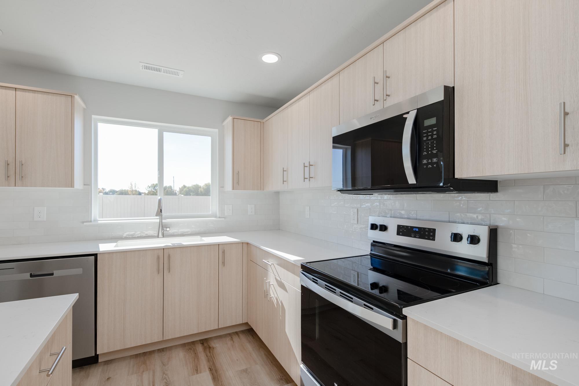 Kitchen with light brown cabinets, stainless steel appliances, light wood-style flooring, light stone countertops, and recessed lighting