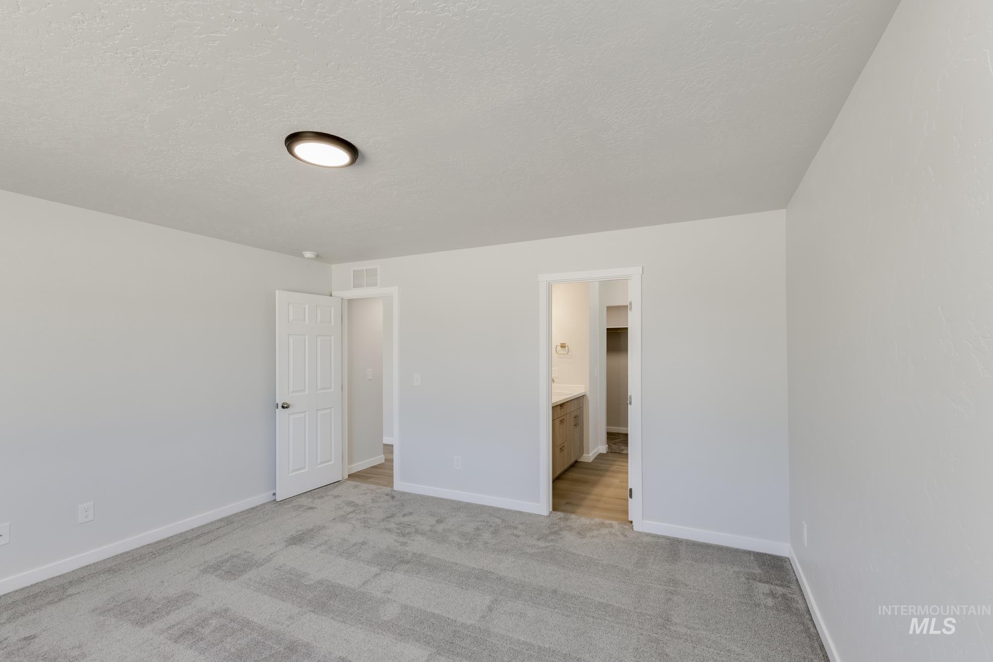 Unfurnished bedroom with light carpet, a textured ceiling, and ensuite bathroom