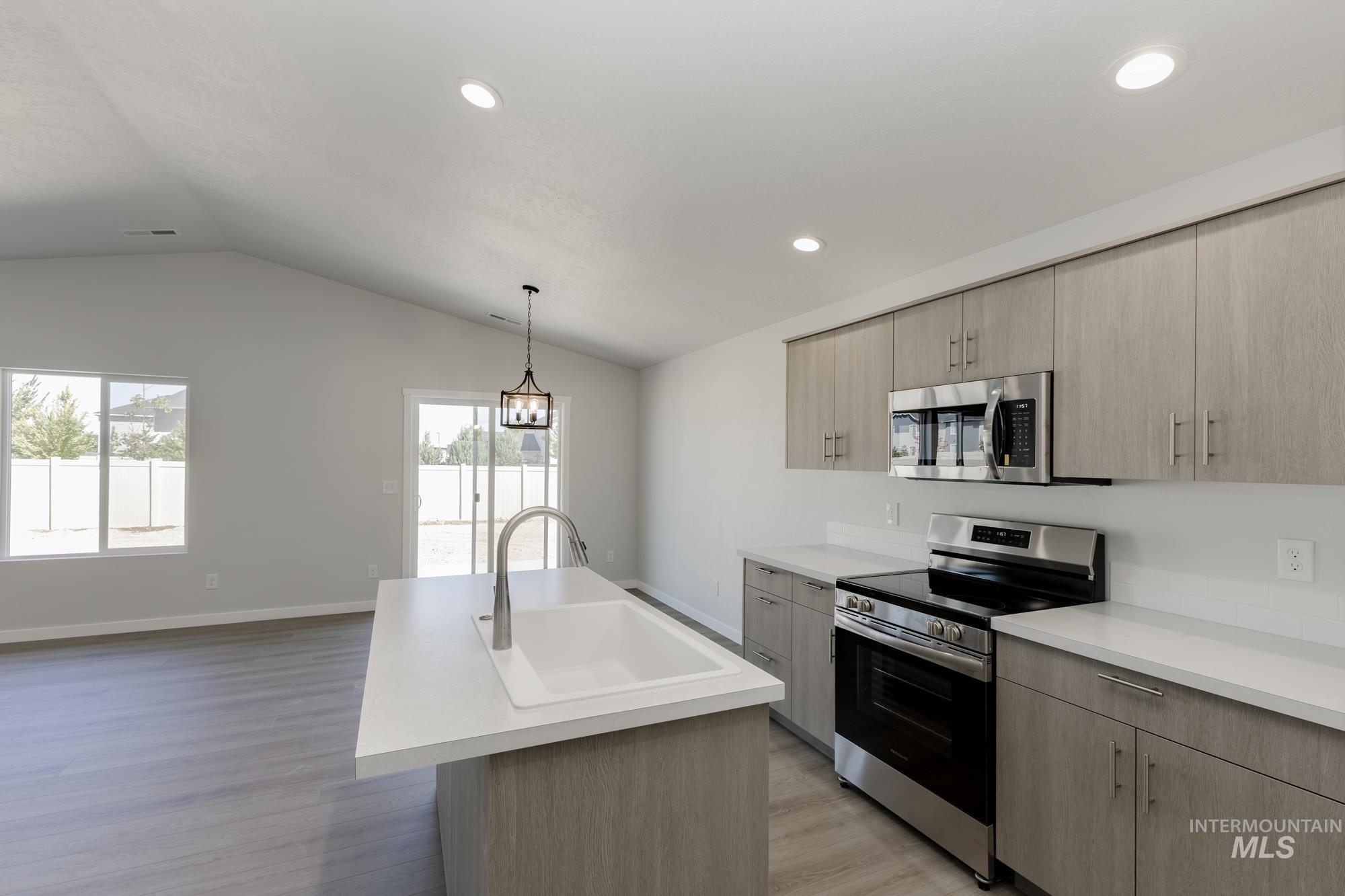 Kitchen featuring appliances with stainless steel finishes, light brown cabinets, light countertops, vaulted ceiling, and a center island with sink