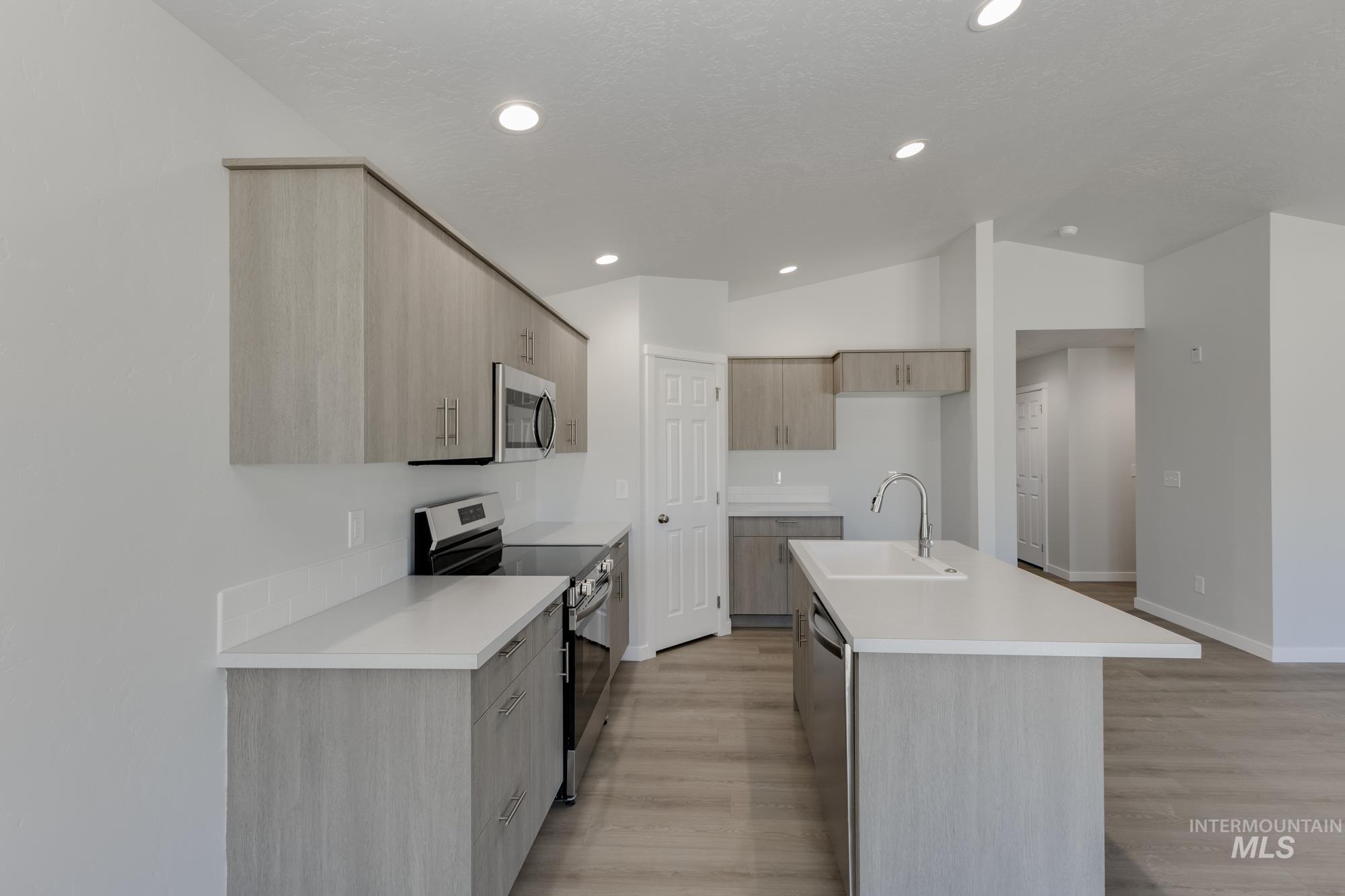 Kitchen featuring appliances with stainless steel finishes, modern cabinets, light countertops, an island with sink, and light brown cabinets