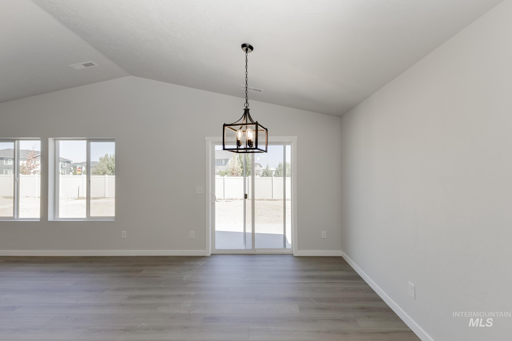 Empty room featuring light wood-style floors, vaulted ceiling, and a chandelier