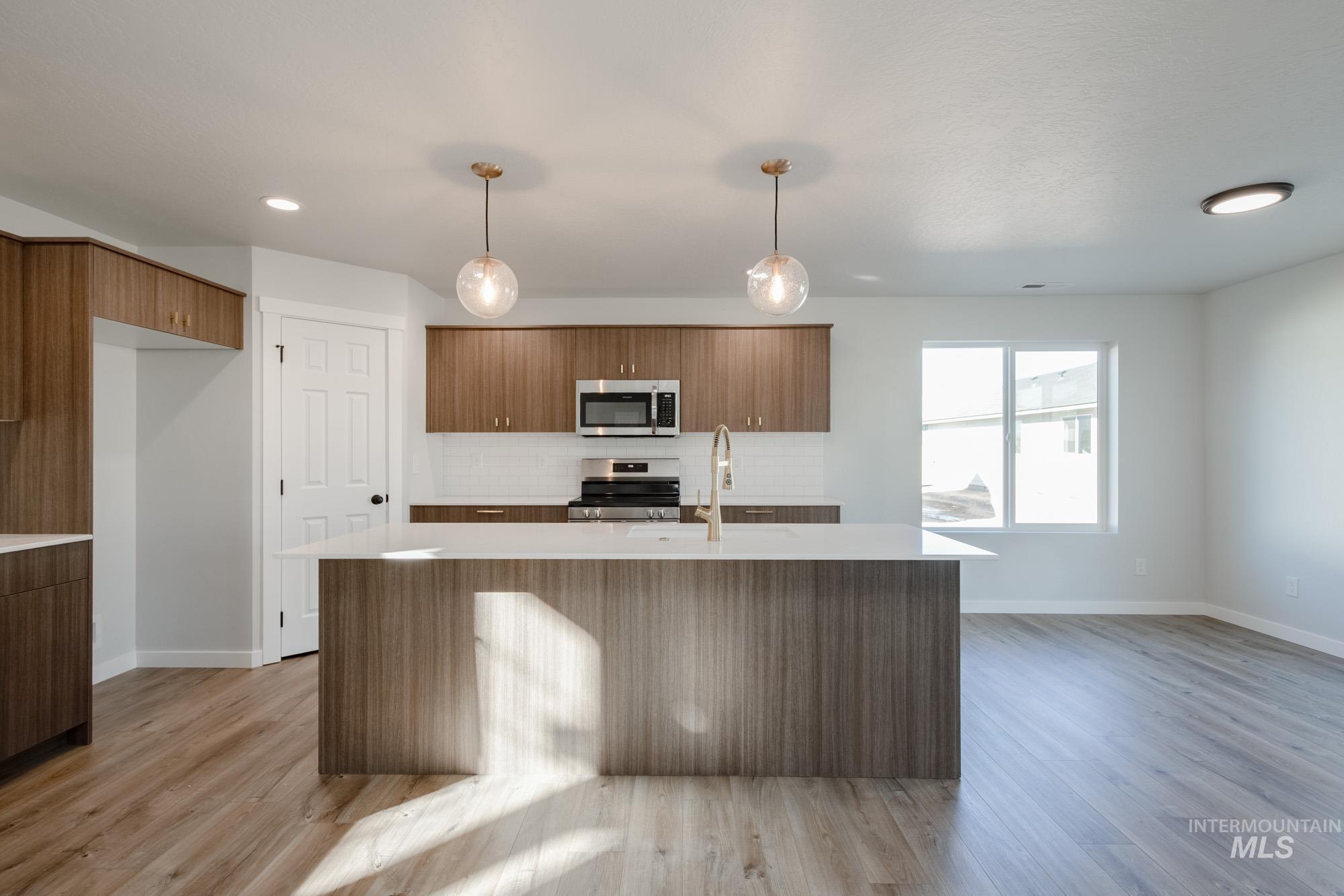 Kitchen with a center island with sink, decorative backsplash, pendant lighting, appliances with stainless steel finishes, and light wood-style flooring