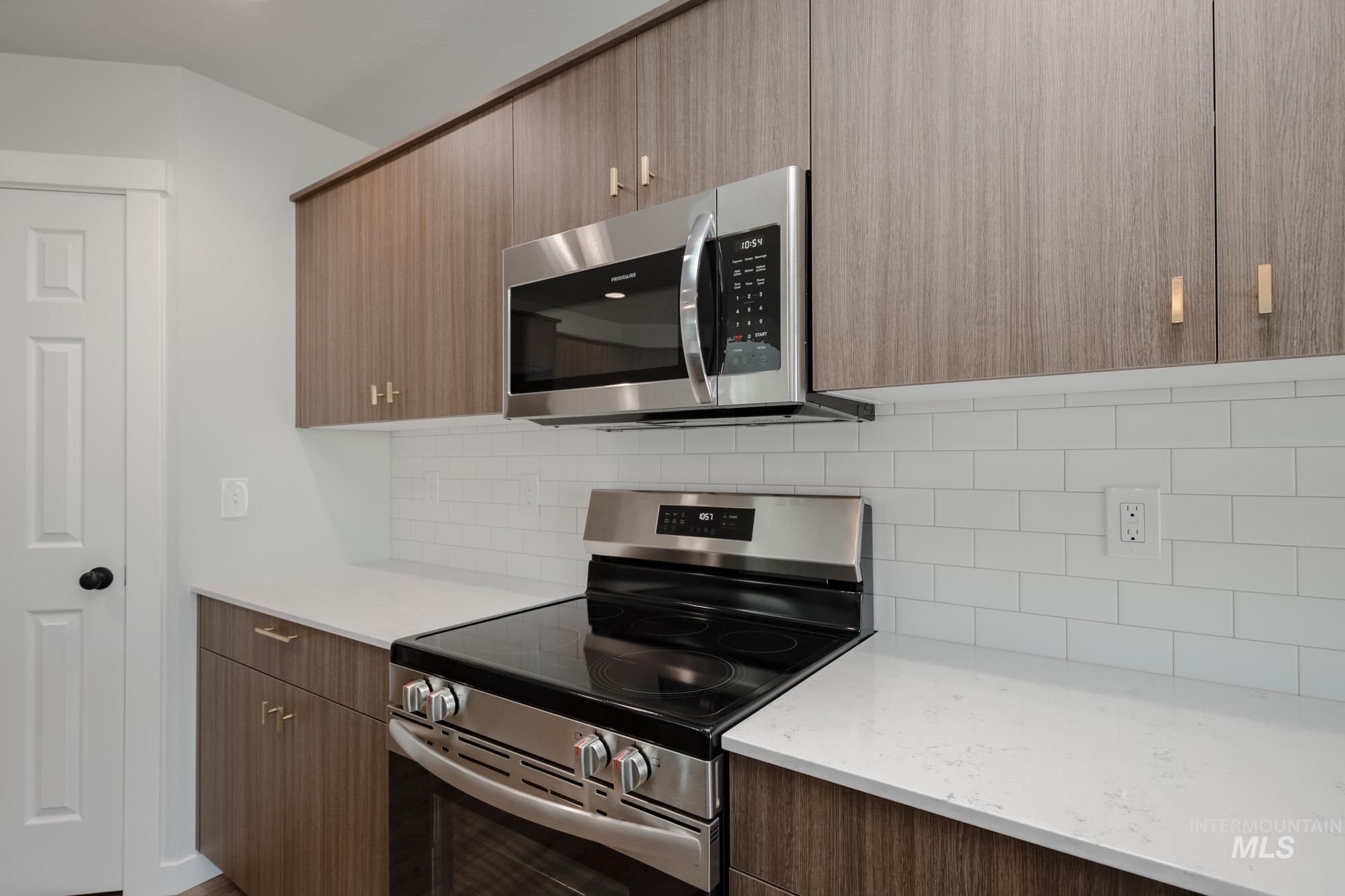 Kitchen featuring appliances with stainless steel finishes, modern cabinets, decorative backsplash, and light stone counters