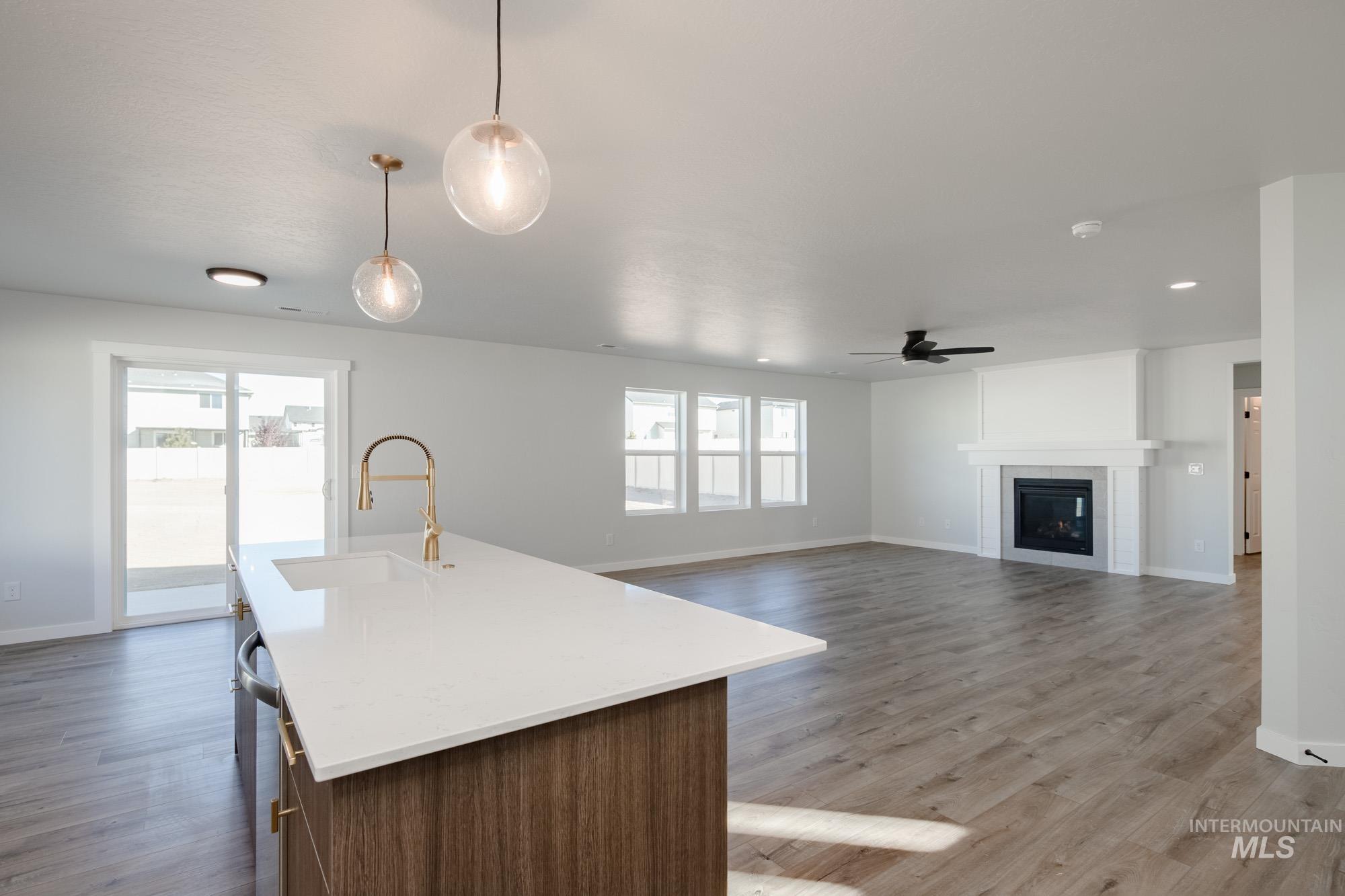 Kitchen featuring open floor plan, a center island with sink, pendant lighting, a tile fireplace, and light stone countertops