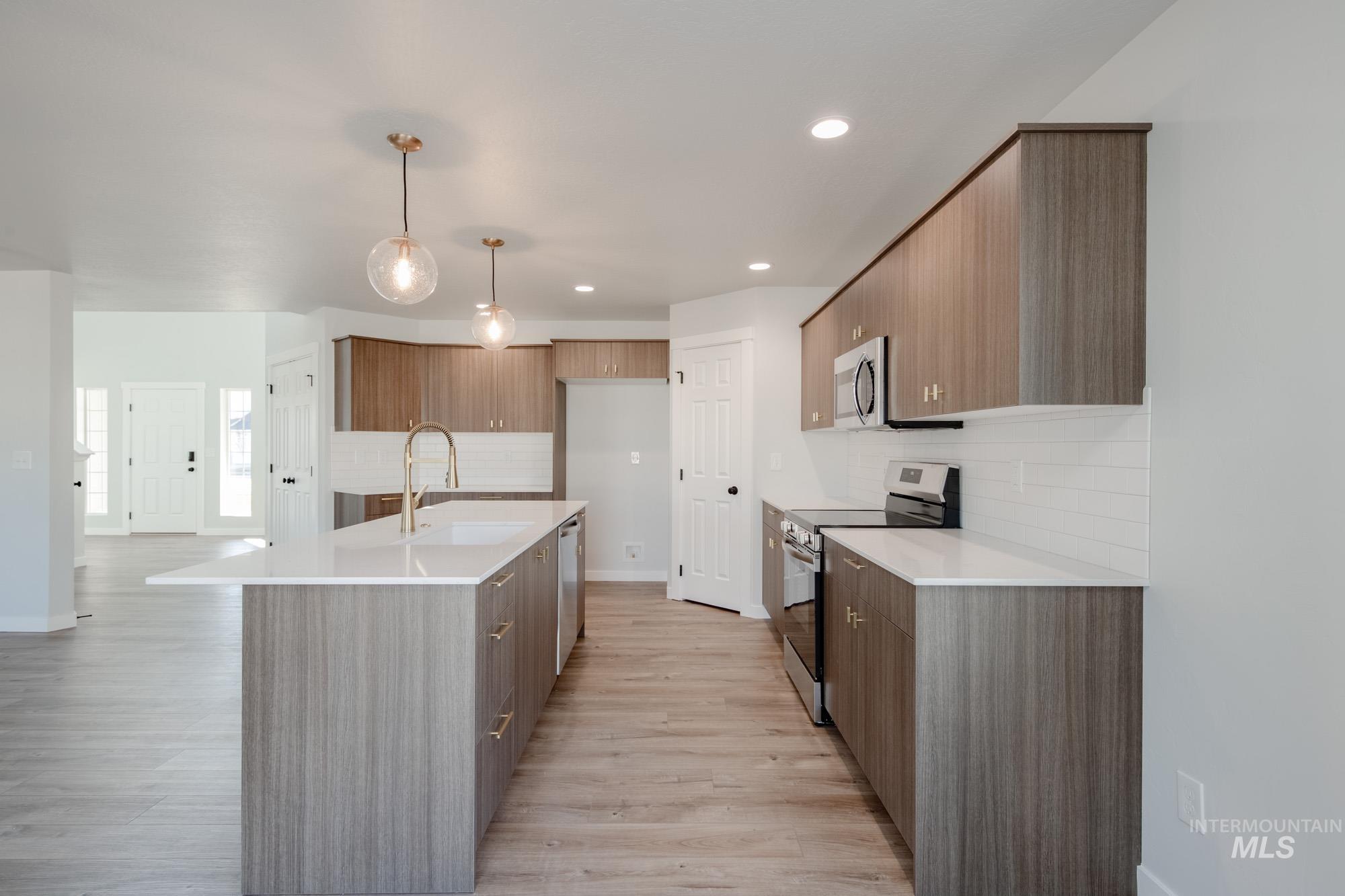 Kitchen featuring modern cabinets, appliances with stainless steel finishes, tasteful backsplash, decorative light fixtures, and a center island with sink