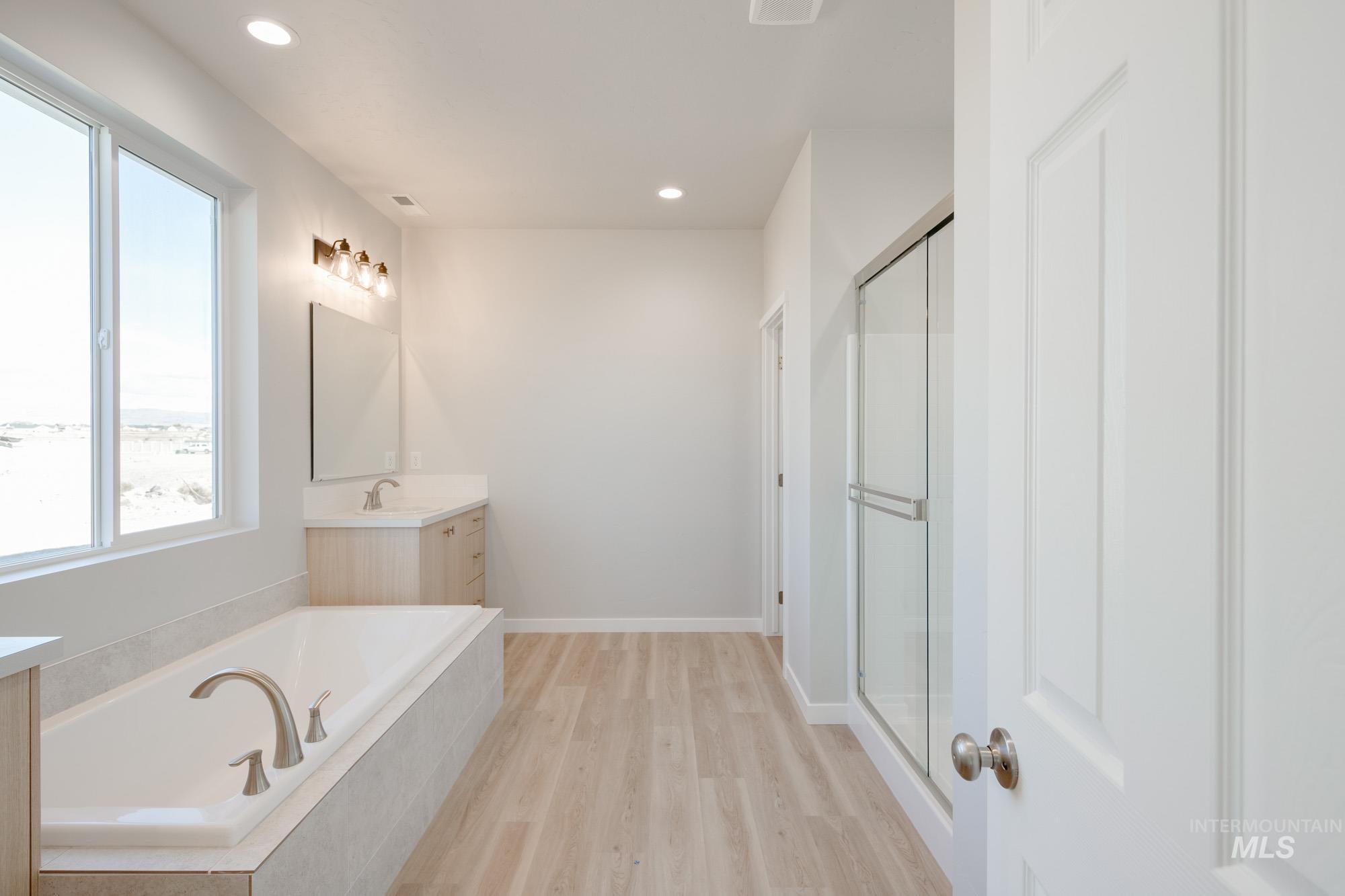 Full bath featuring vanity, a bath, light wood finished floors, a stall shower, and recessed lighting