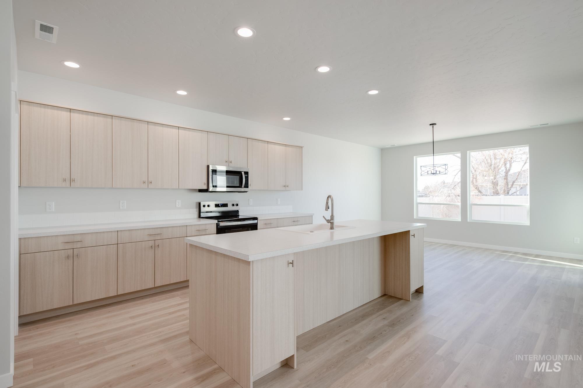 Kitchen with light brown cabinetry, an island with sink, stainless steel appliances, recessed lighting, and light wood-type flooring