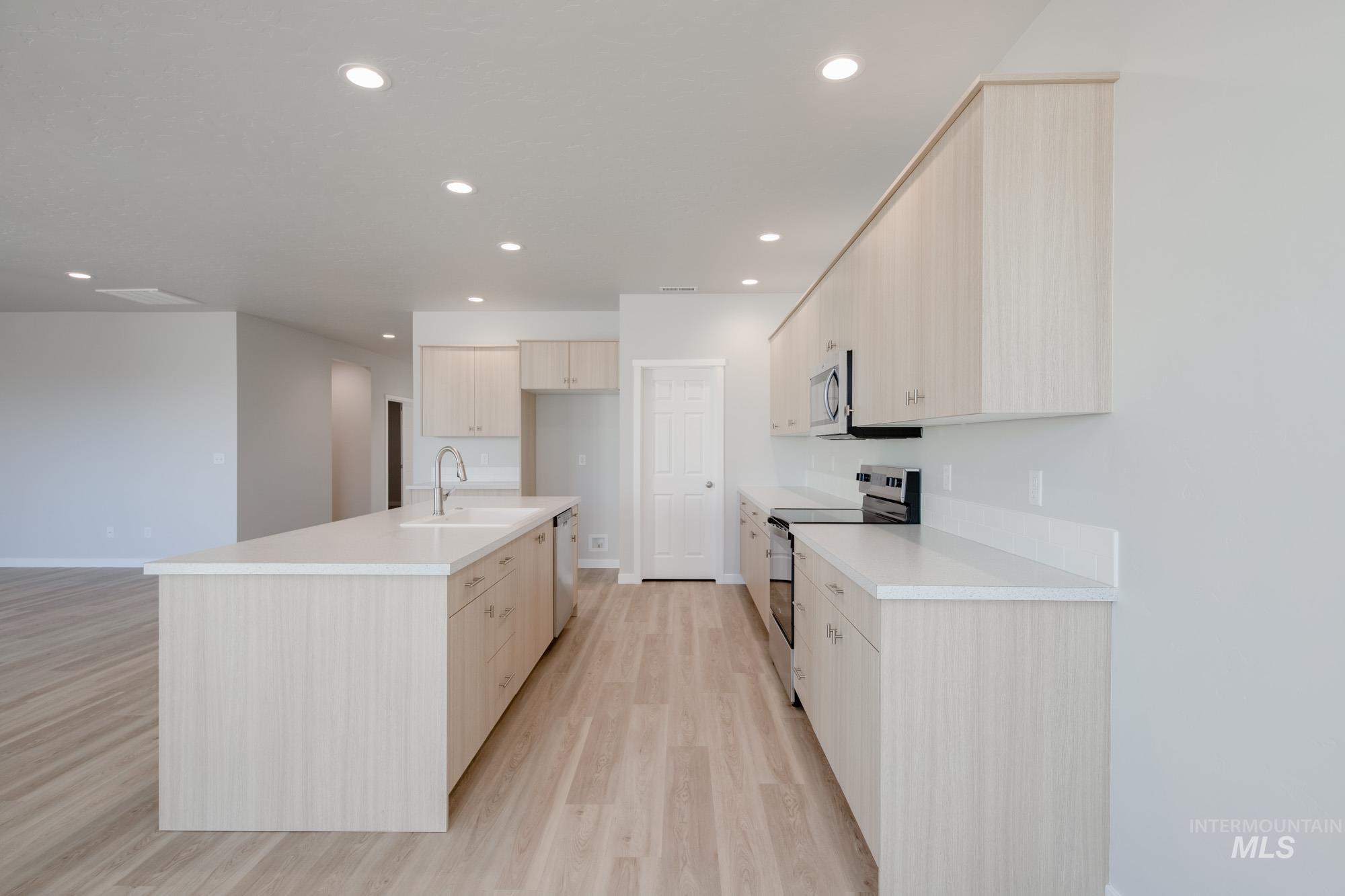 Kitchen with appliances with stainless steel finishes, light brown cabinets, light wood-type flooring, a center island with sink, and recessed lighting