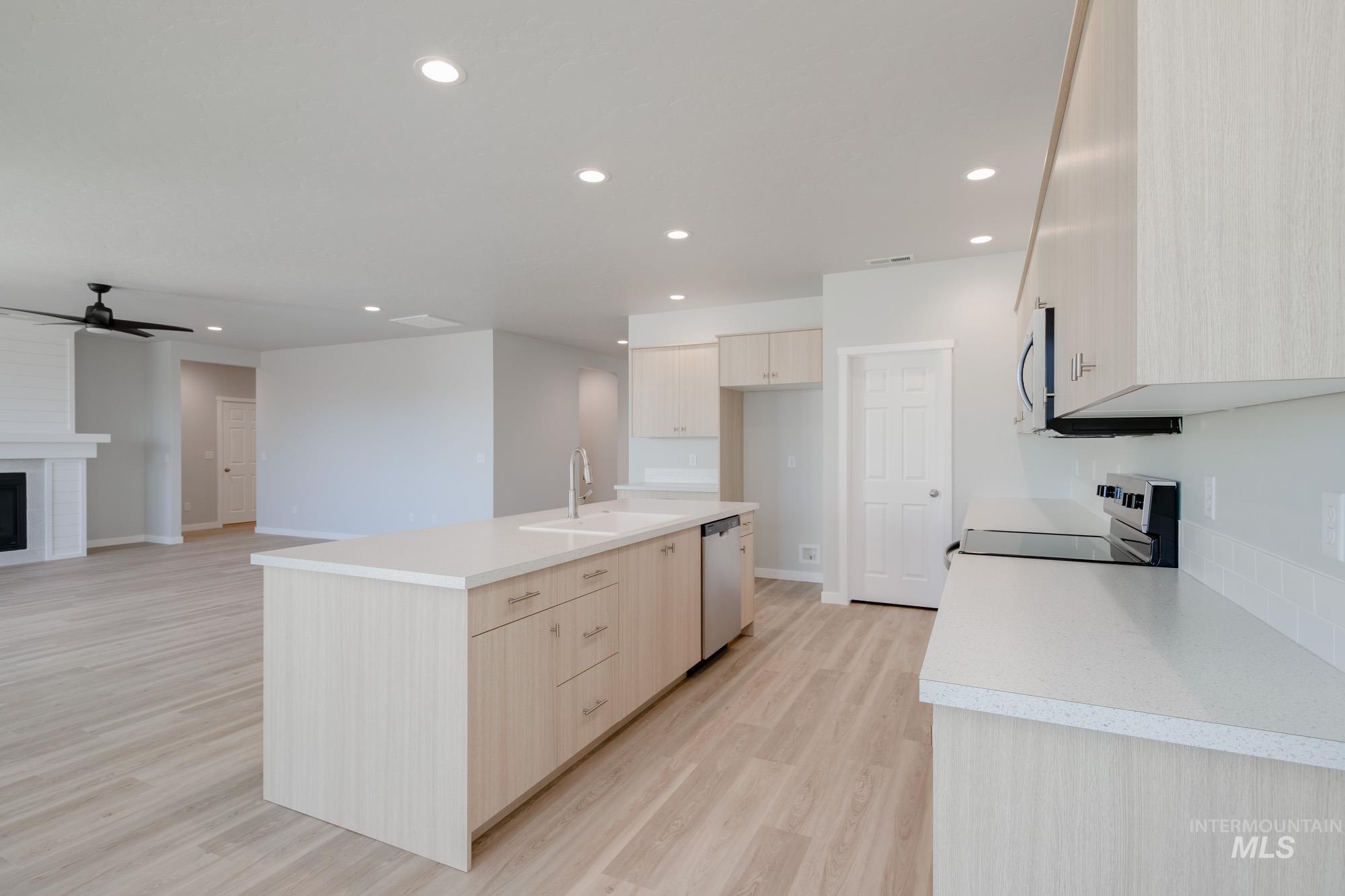 Kitchen featuring light countertops, a kitchen island with sink, light brown cabinets, light wood-type flooring, and stainless steel appliances