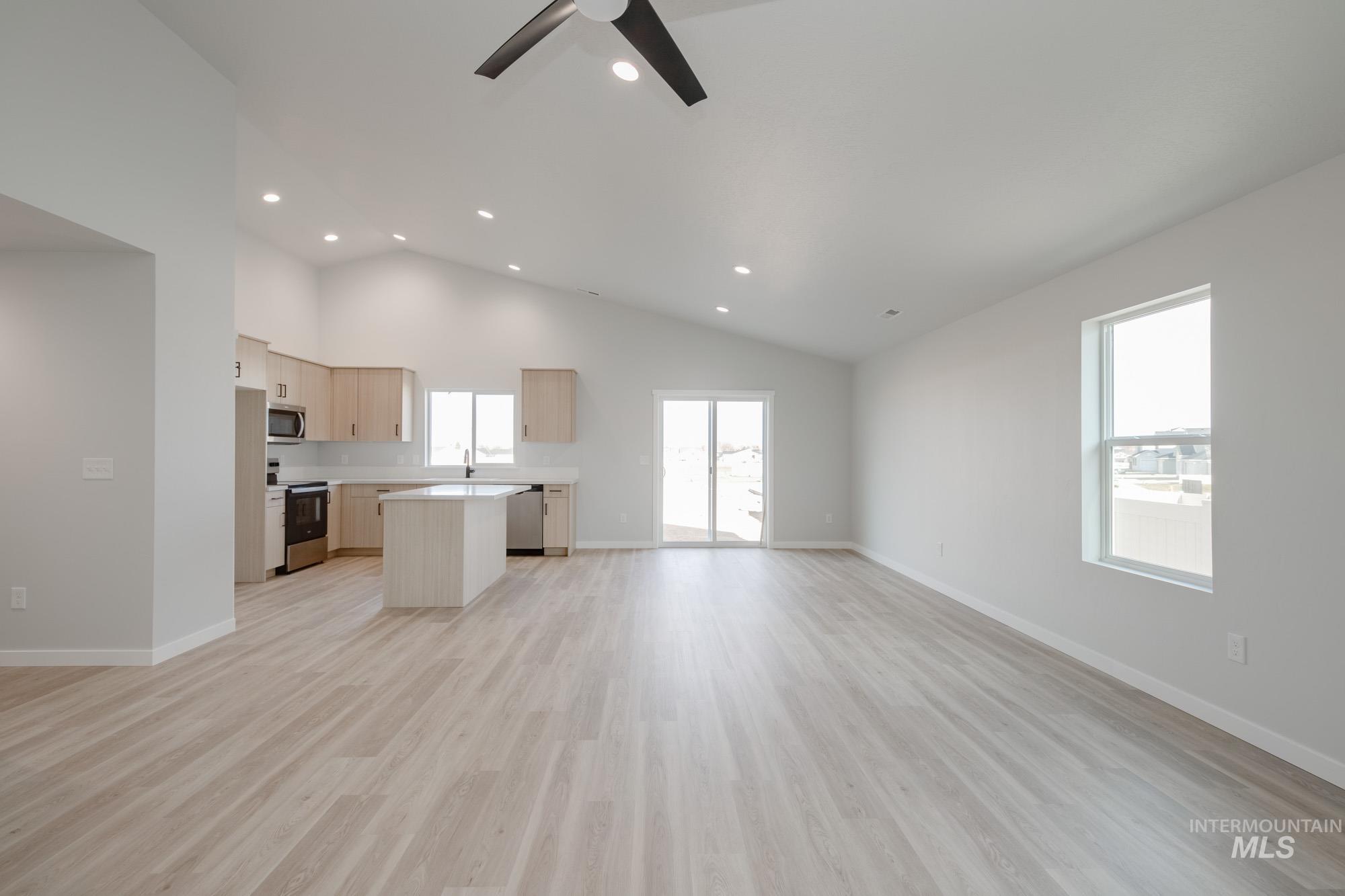 Kitchen with open floor plan, light brown cabinets, a kitchen island, light countertops, and appliances with stainless steel finishes