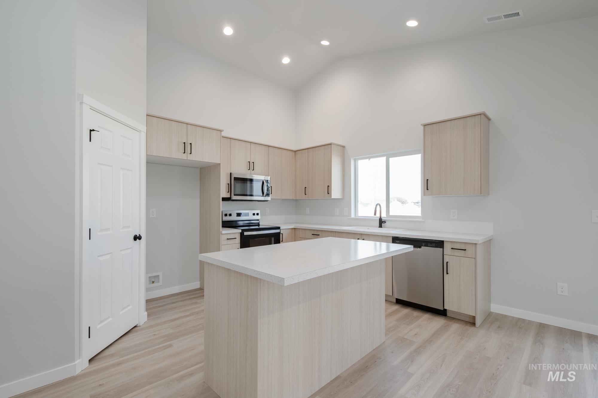 Kitchen with light brown cabinets, stainless steel appliances, light countertops, a center island, and high vaulted ceiling