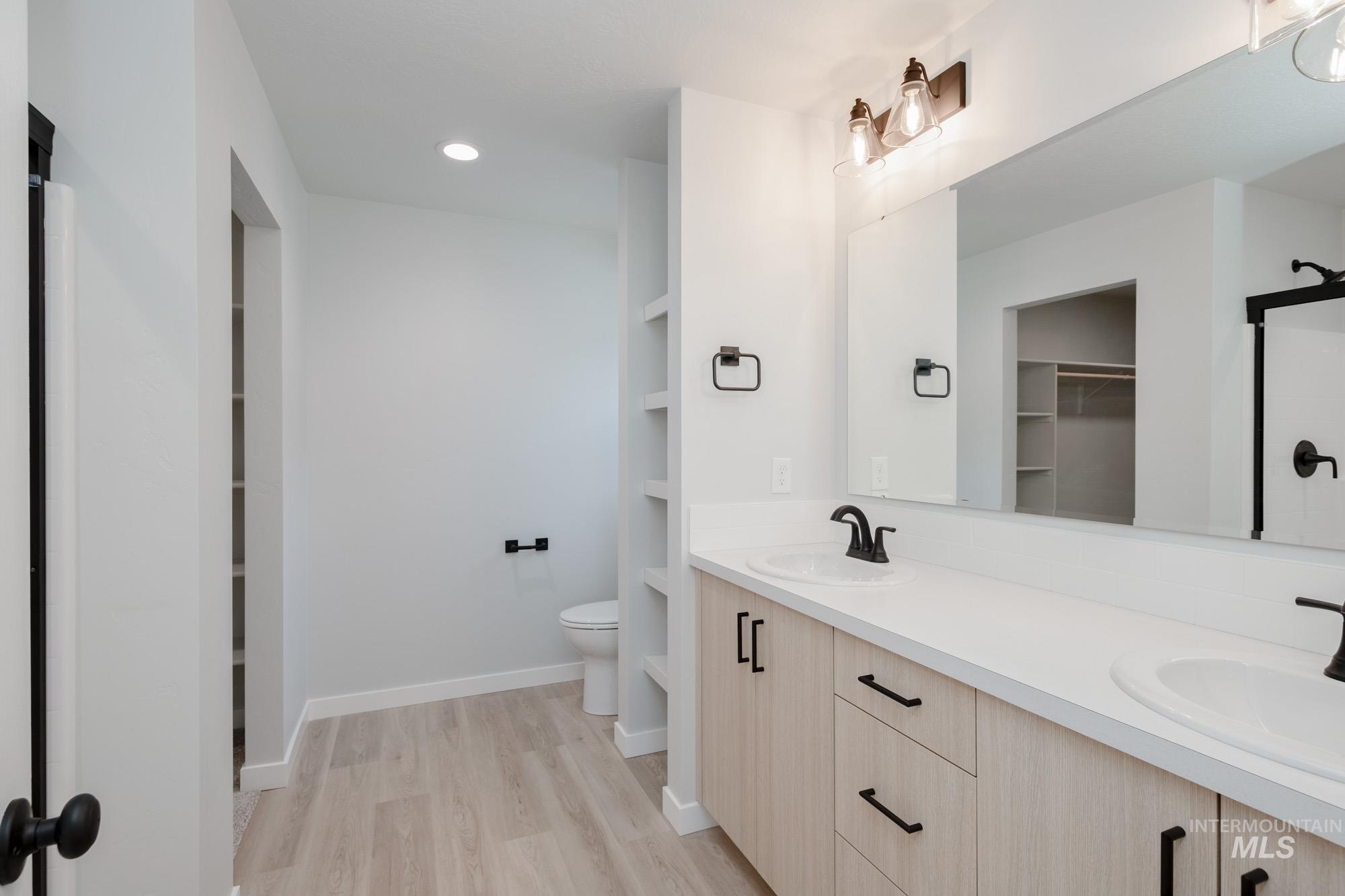 Full bathroom featuring a shower stall, double vanity, a walk in closet, light wood finished floors, and recessed lighting