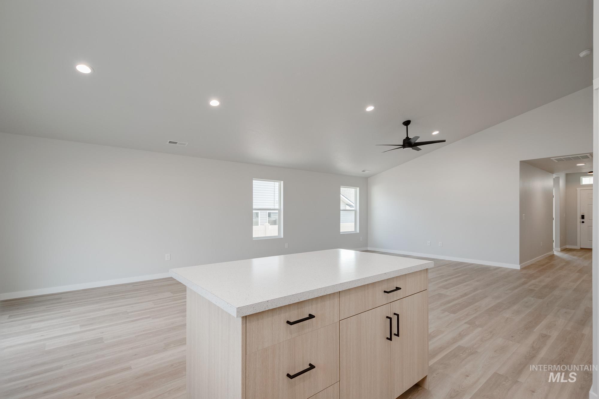 Kitchen with light brown cabinetry, a center island, open floor plan, lofted ceiling, and recessed lighting