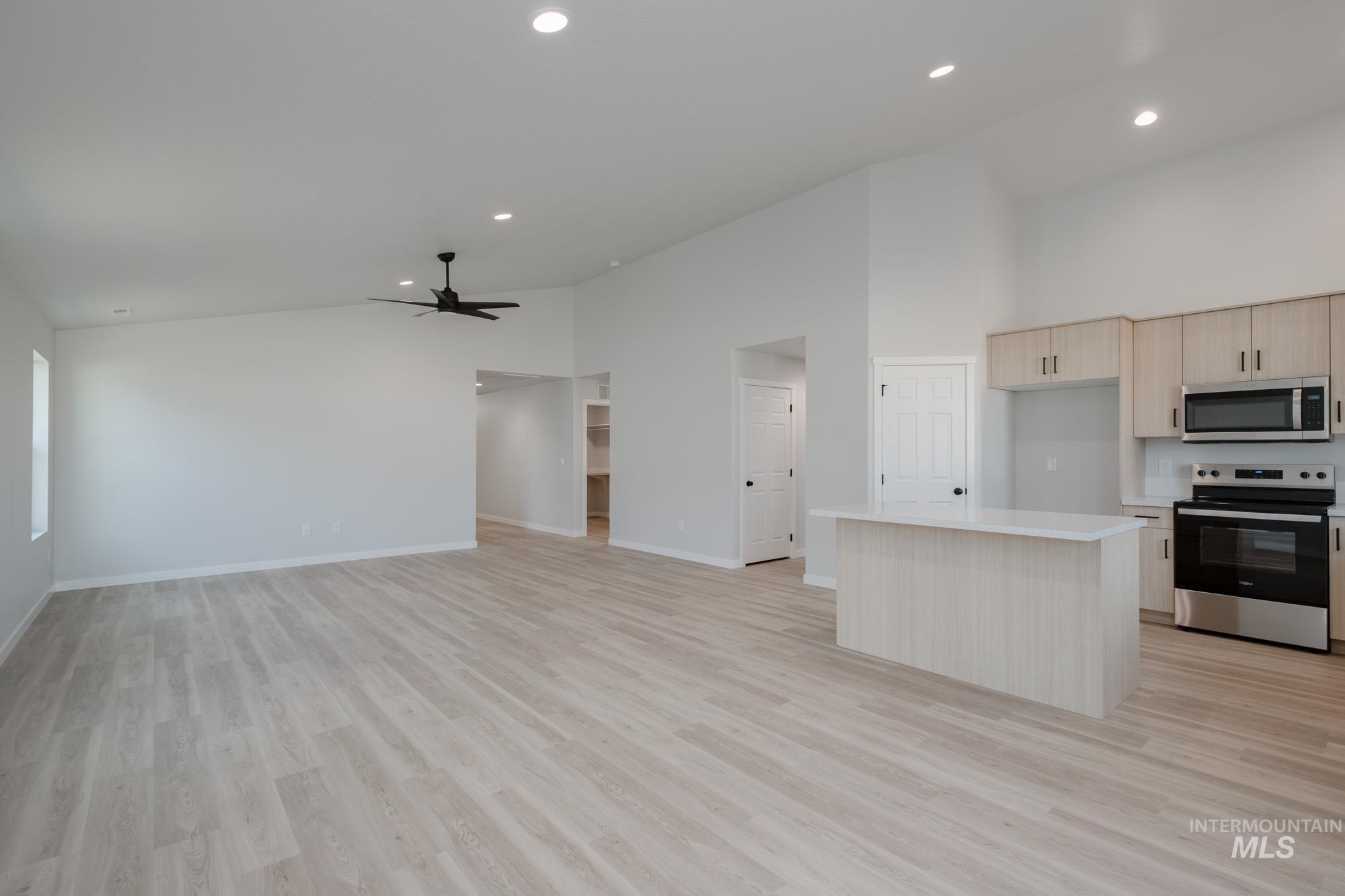 Kitchen with a center island, stainless steel appliances, high vaulted ceiling, light wood finished floors, and open floor plan