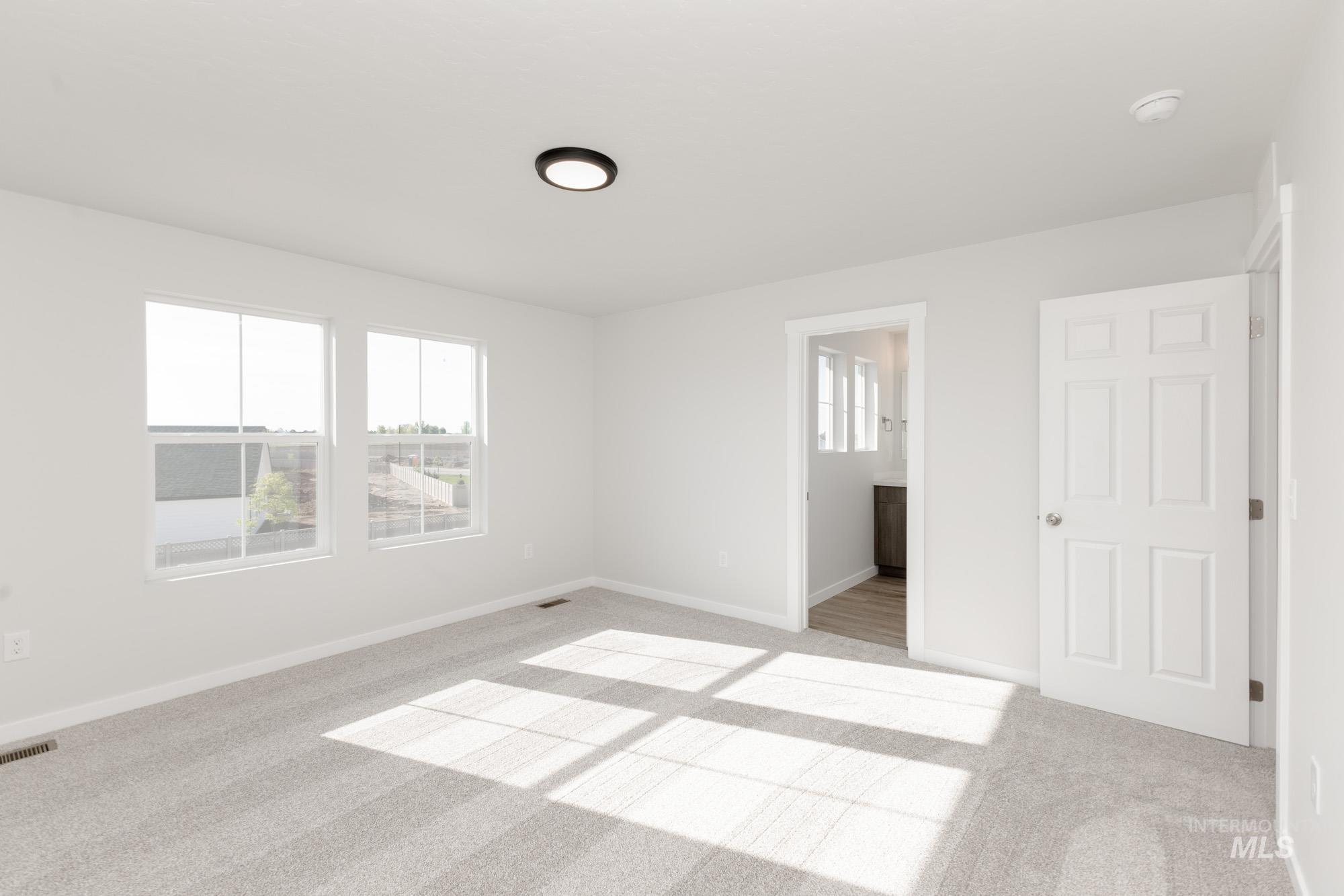 Unfurnished bedroom with light colored carpet, multiple windows, and ensuite bathroom