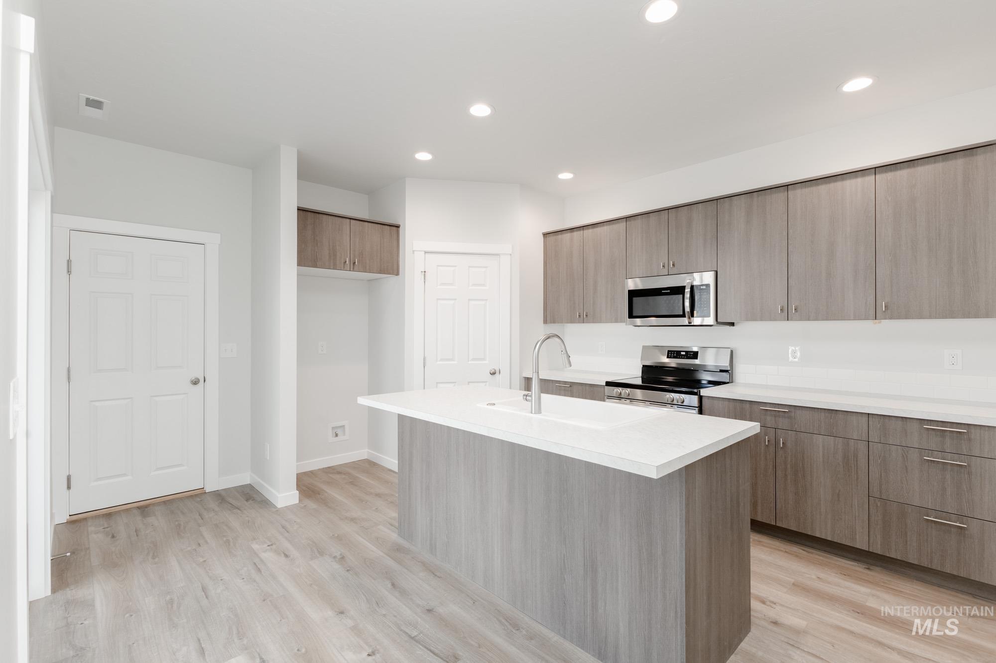 Kitchen featuring light countertops, stainless steel appliances, light wood-type flooring, a kitchen island with sink, and modern cabinets