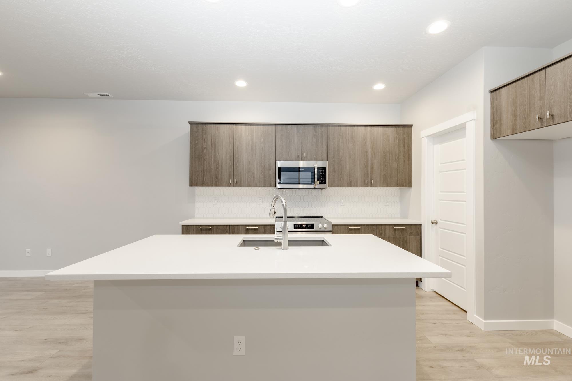 Kitchen featuring appliances with stainless steel finishes, an island with sink, modern cabinets, light wood finished floors, and brown cabinets