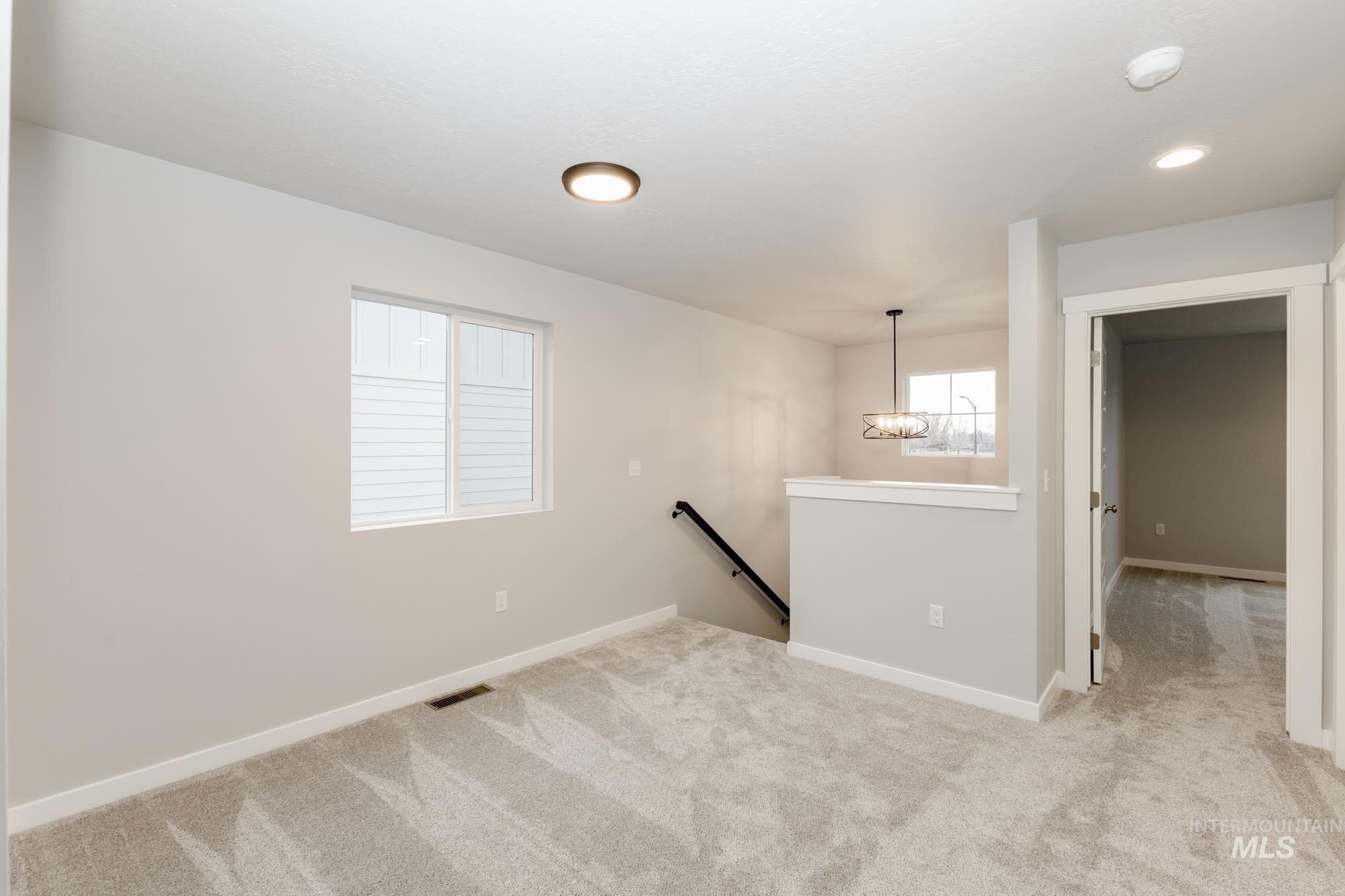 Empty room with light colored carpet, a chandelier, and recessed lighting